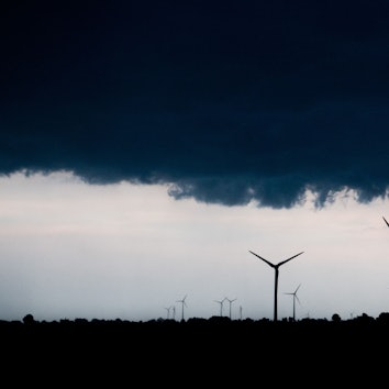 Mehrere Windräder ragen in den Himmel, der von Regenwolken verdunkelt ist.