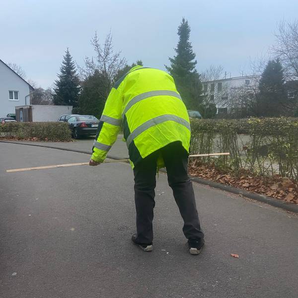 Ein Mann in einer gelben Warnweste prüft mit dem Zollstock, ob die Durchfahrtsbreite für Müllwagen reicht.