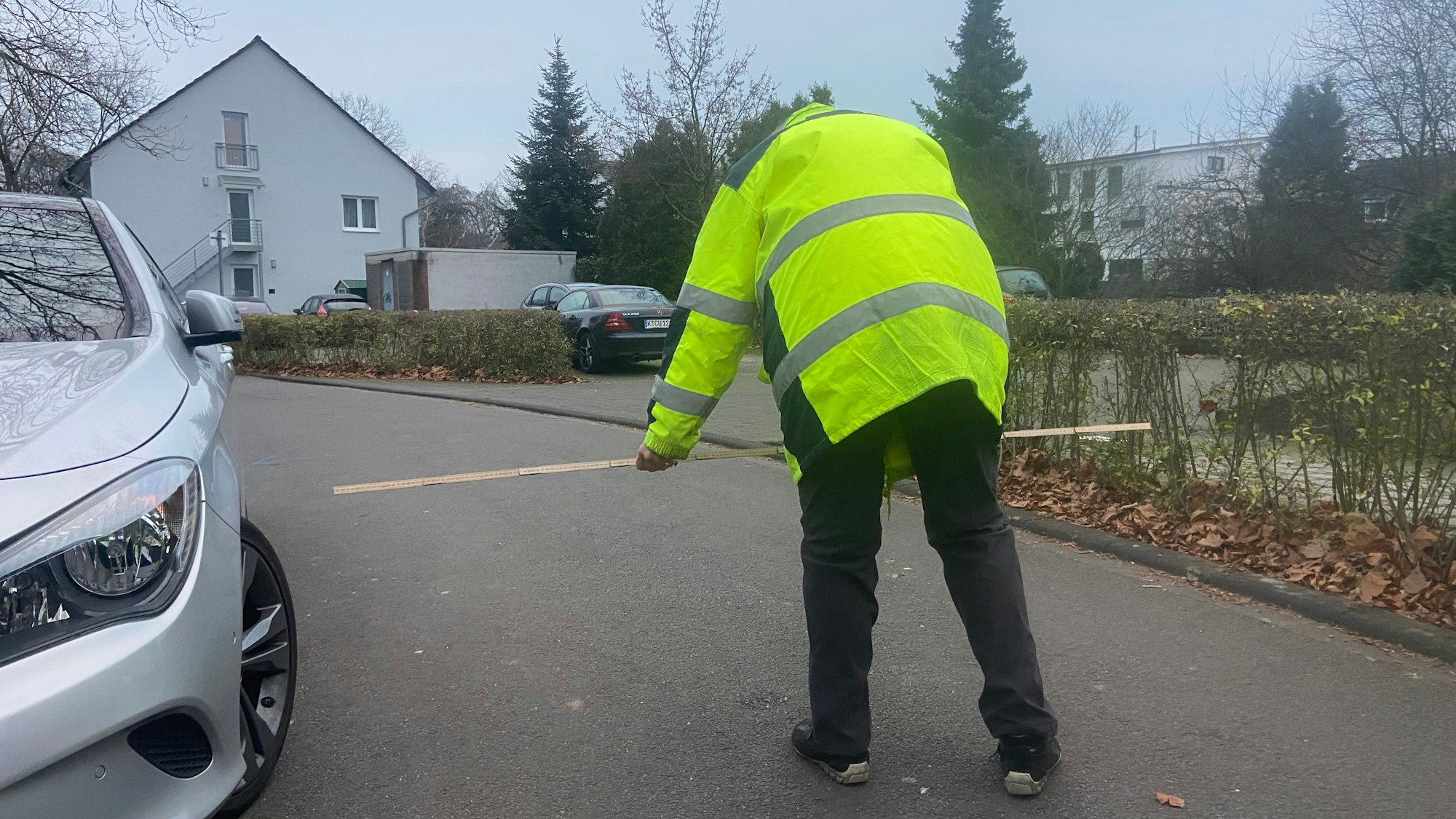 Ein Mann in einer gelben Warnweste prüft mit dem Zollstock, ob die Durchfahrtsbreite für Müllwagen reicht.