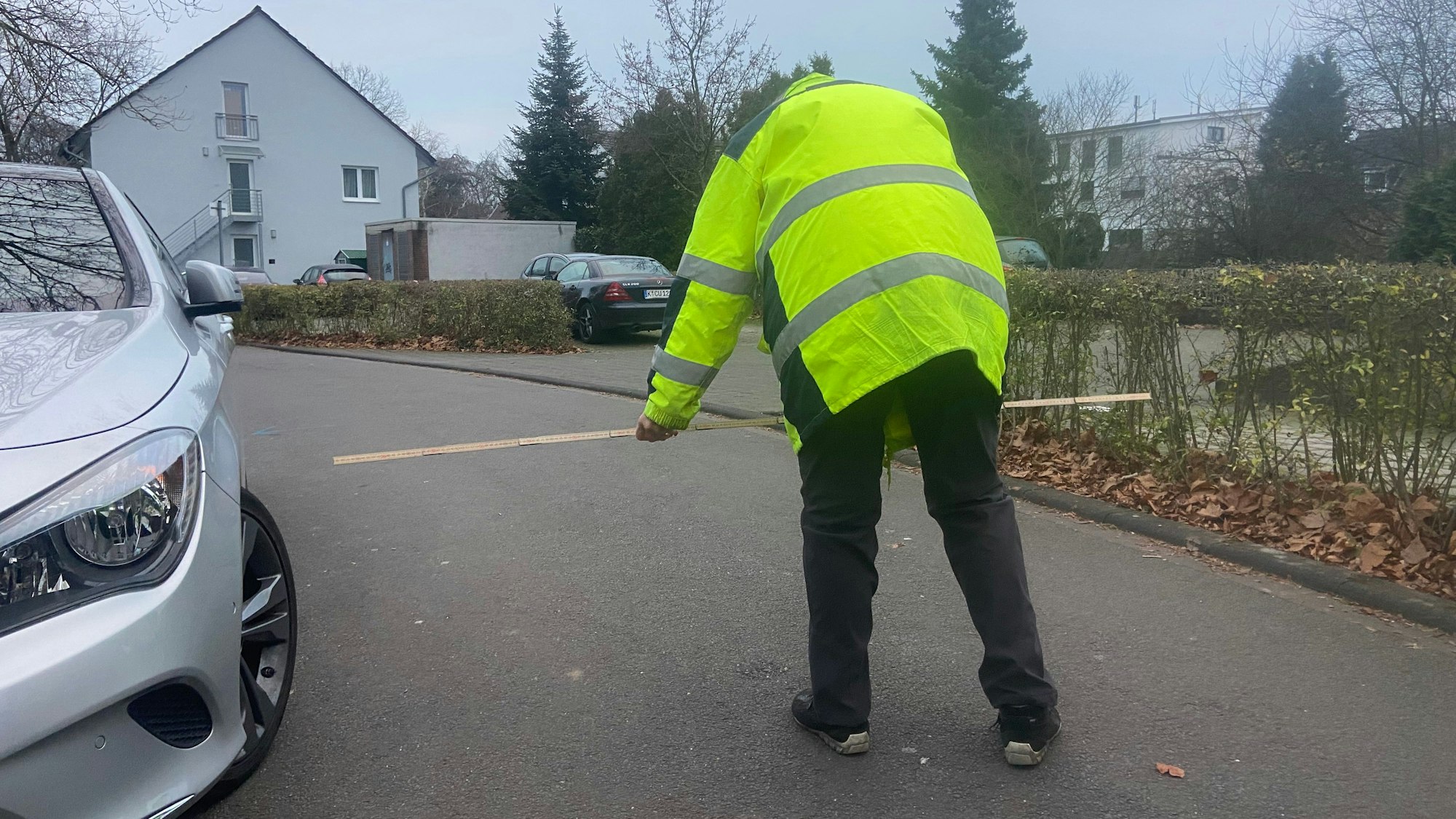 Ein Mann in einer gelben Warnweste prüft mit dem Zollstock, ob die Durchfahrtsbreite für Müllwagen reicht.