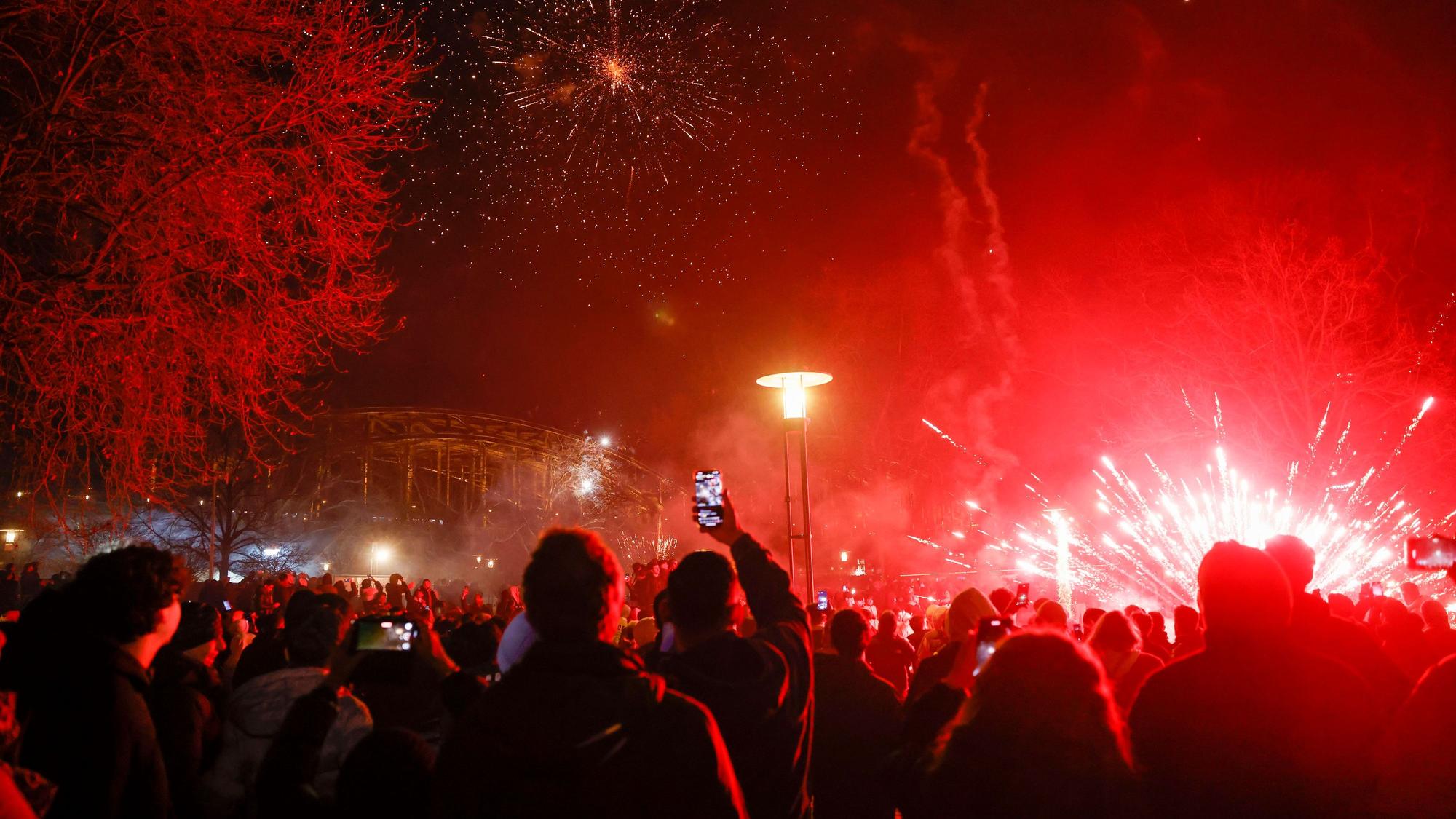 Menschenmengen stehen im Rheingarten. Feuerwerk färbt alles in rot ein.