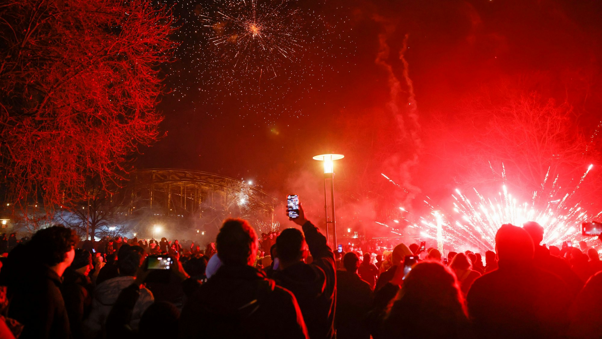 Menschenmengen stehen im Rheingarten. Feuerwerk färbt alles in rot ein.