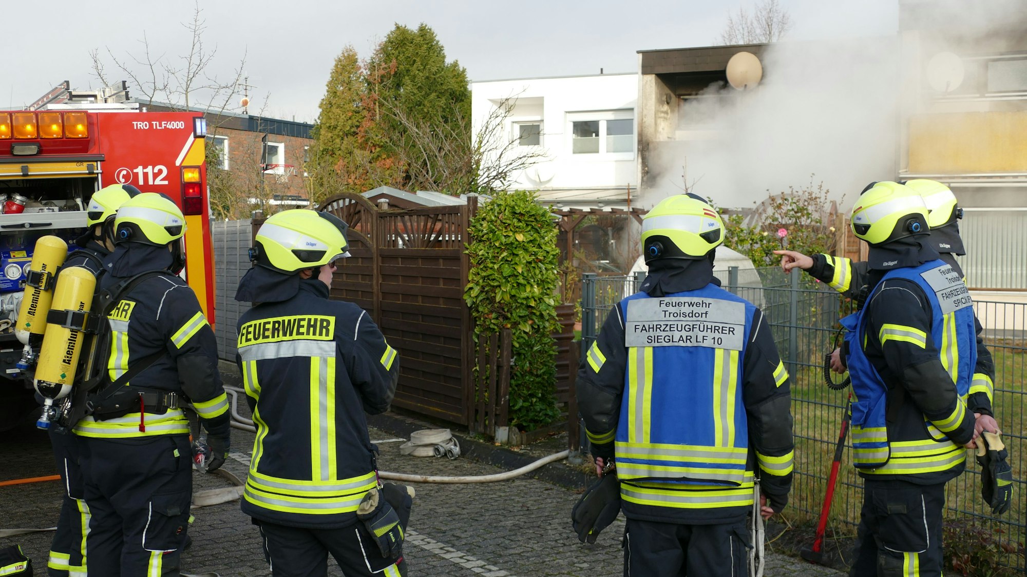 Feuerwehrleute stehen auf der Rückseite des brennenden Hauses.