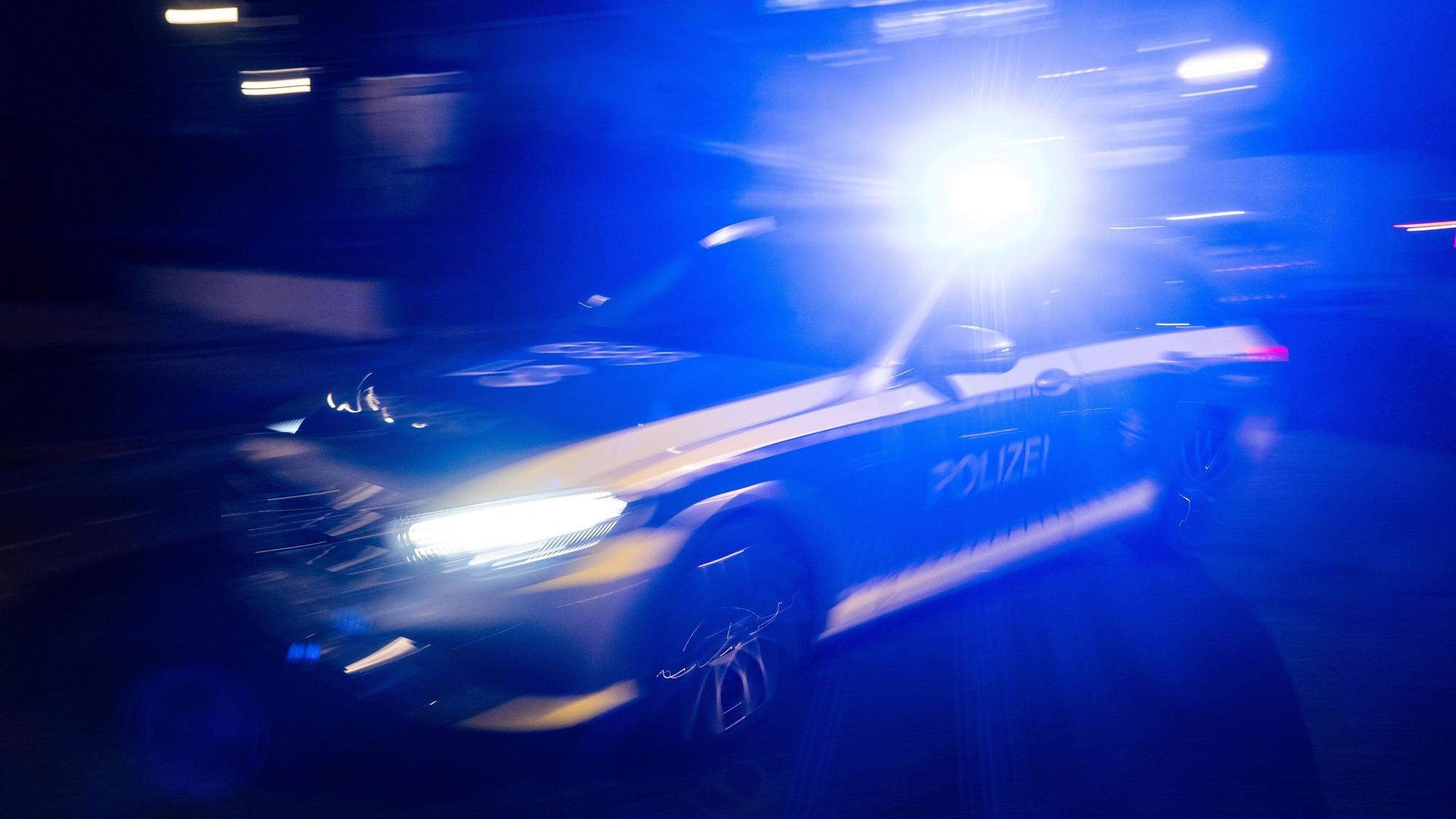 Ein Polizeifahrzeug fährt mit Blaulicht an einem Gebäude vorbei.
