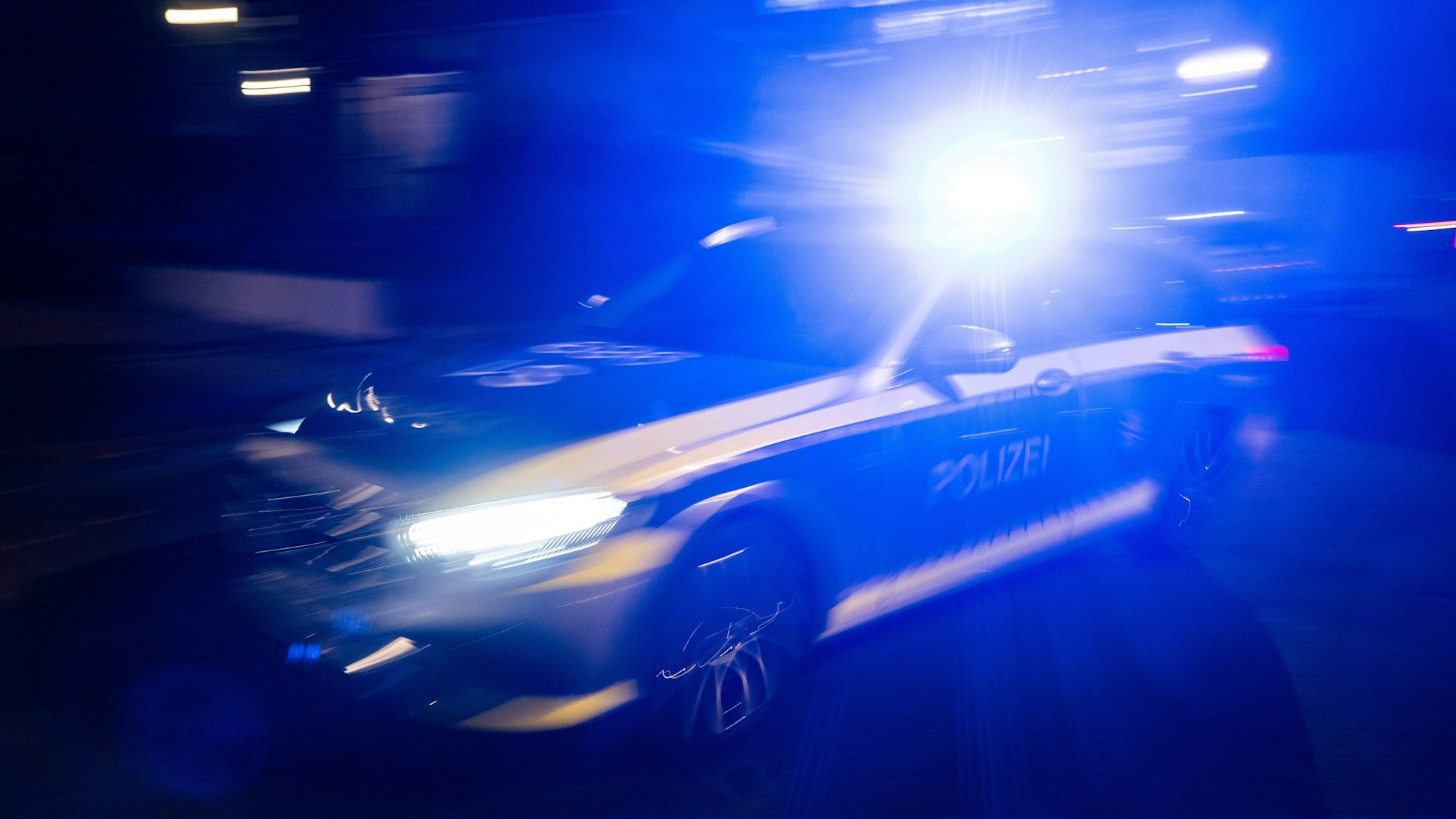Ein Polizeifahrzeug fährt mit Blaulicht an einem Gebäude vorbei.