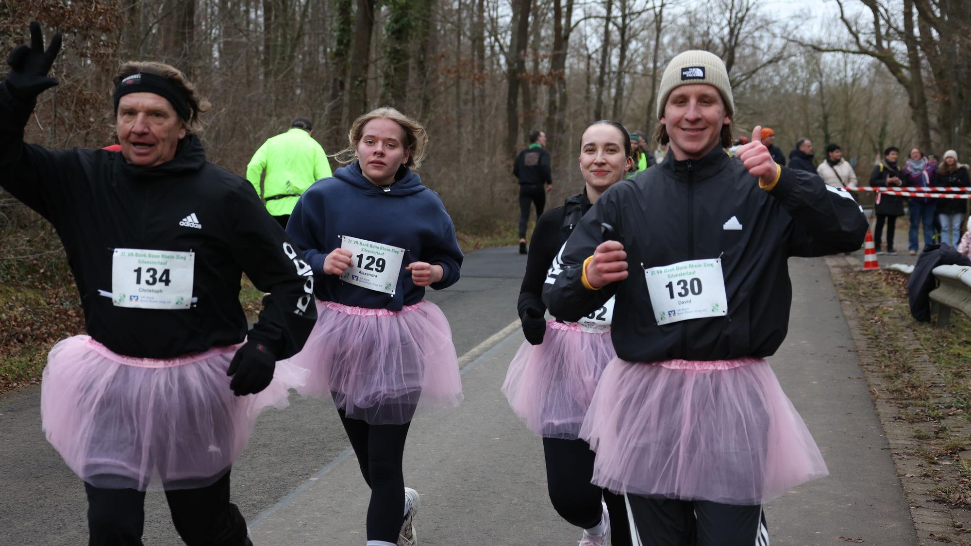 Eine vierköpfige Familie tritt beim Silvesterlauf in rosa Tütüs an. Die Mutter zeigt den erhobenen Daumen, der Vater macht das Victory-Zeichen.