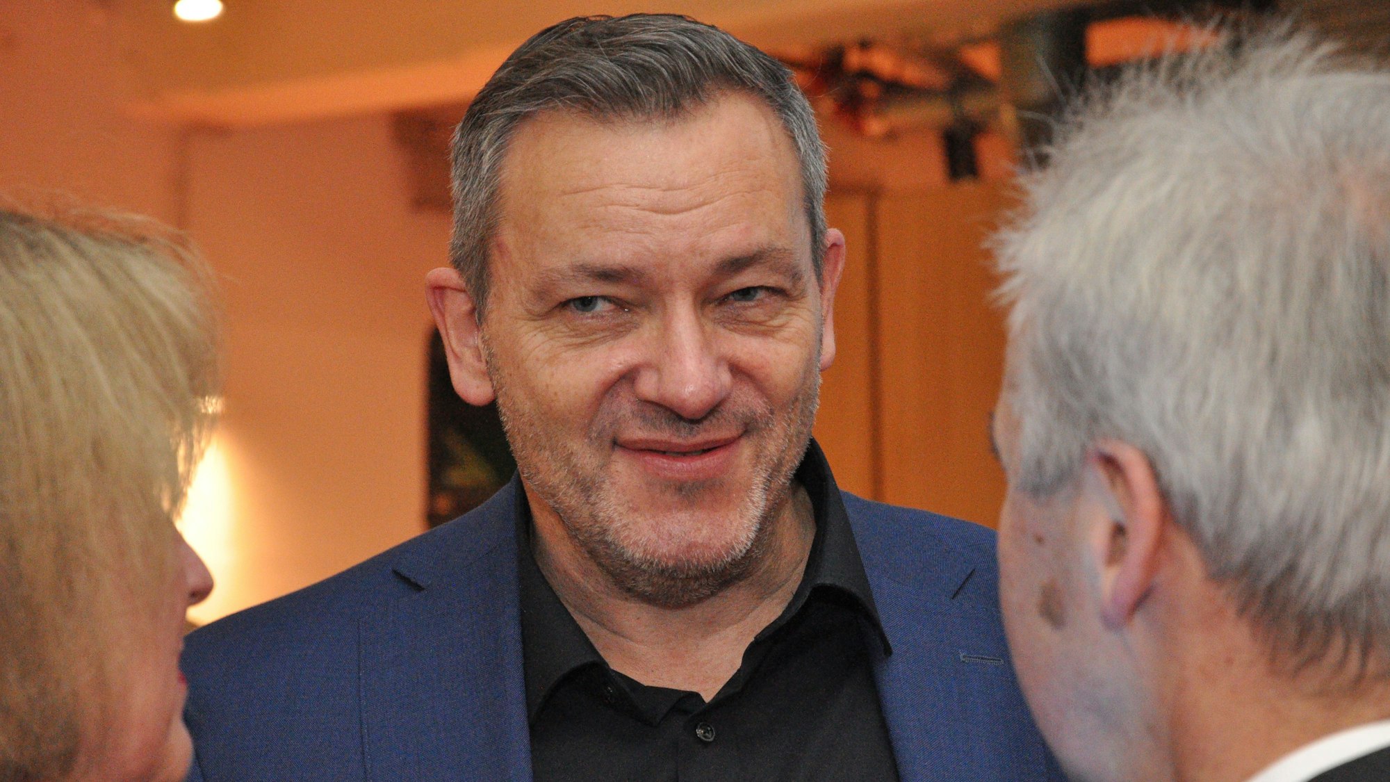 Das Bild zeigt einen Mann in der Mitte, dem eine Frau und ein Mann interessiert zu hören.