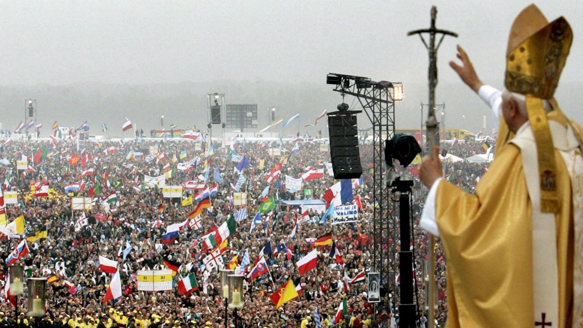 Papst Benedikt XVI. winkt einer Menschenmenge, in der zahlreiche Fahnen geschwenkt werden, von erhöhter Stelle aus zu.