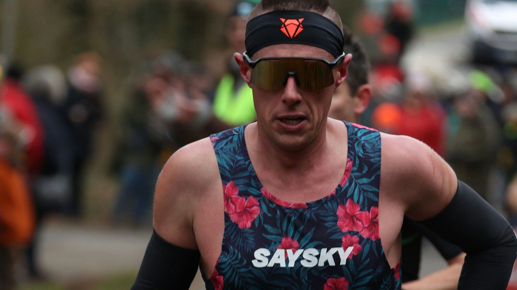 Ein Läufer mit dunkler Sonnenbrille, schwarzem Stirnband, schwarzen Armstulpen und geblümten Sporttrikot beim Silvesterlauf.