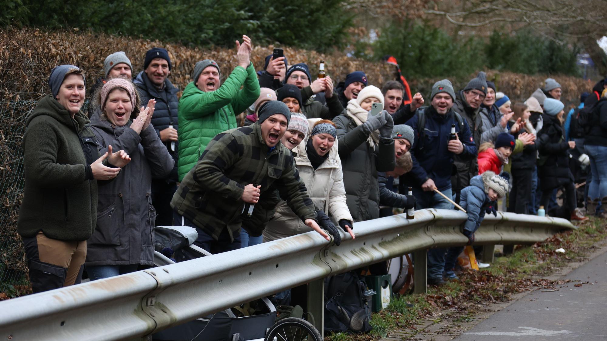 Hinter einer Leitplanke stehen viele Besucher, die die Läufer anfeuern.