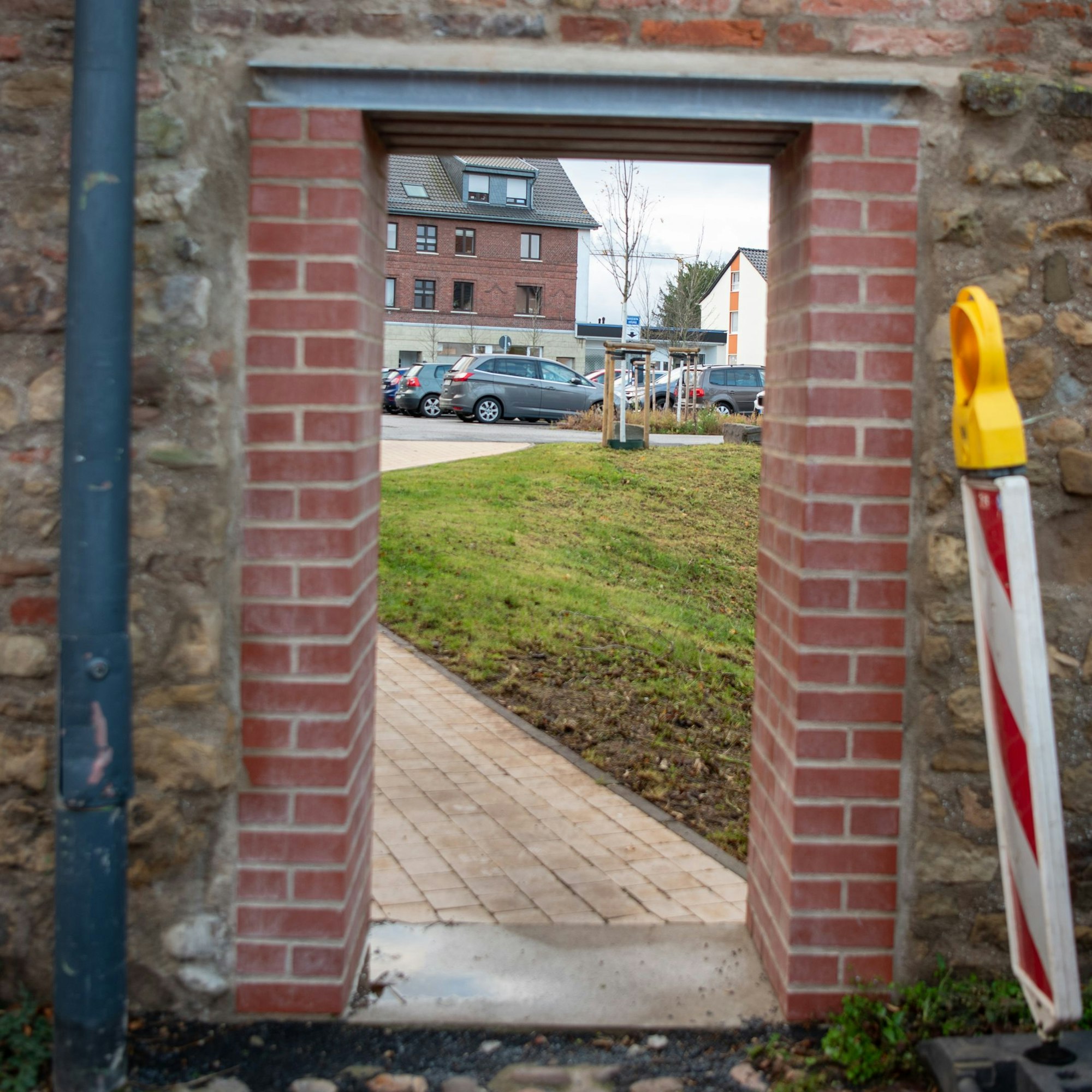 Das Bild zeigt einen Durchgang (Schlupfpforte) durch eine Mauer zu einem Parkplatz, rechts im Bild sind Warnbaken zu sehen.
