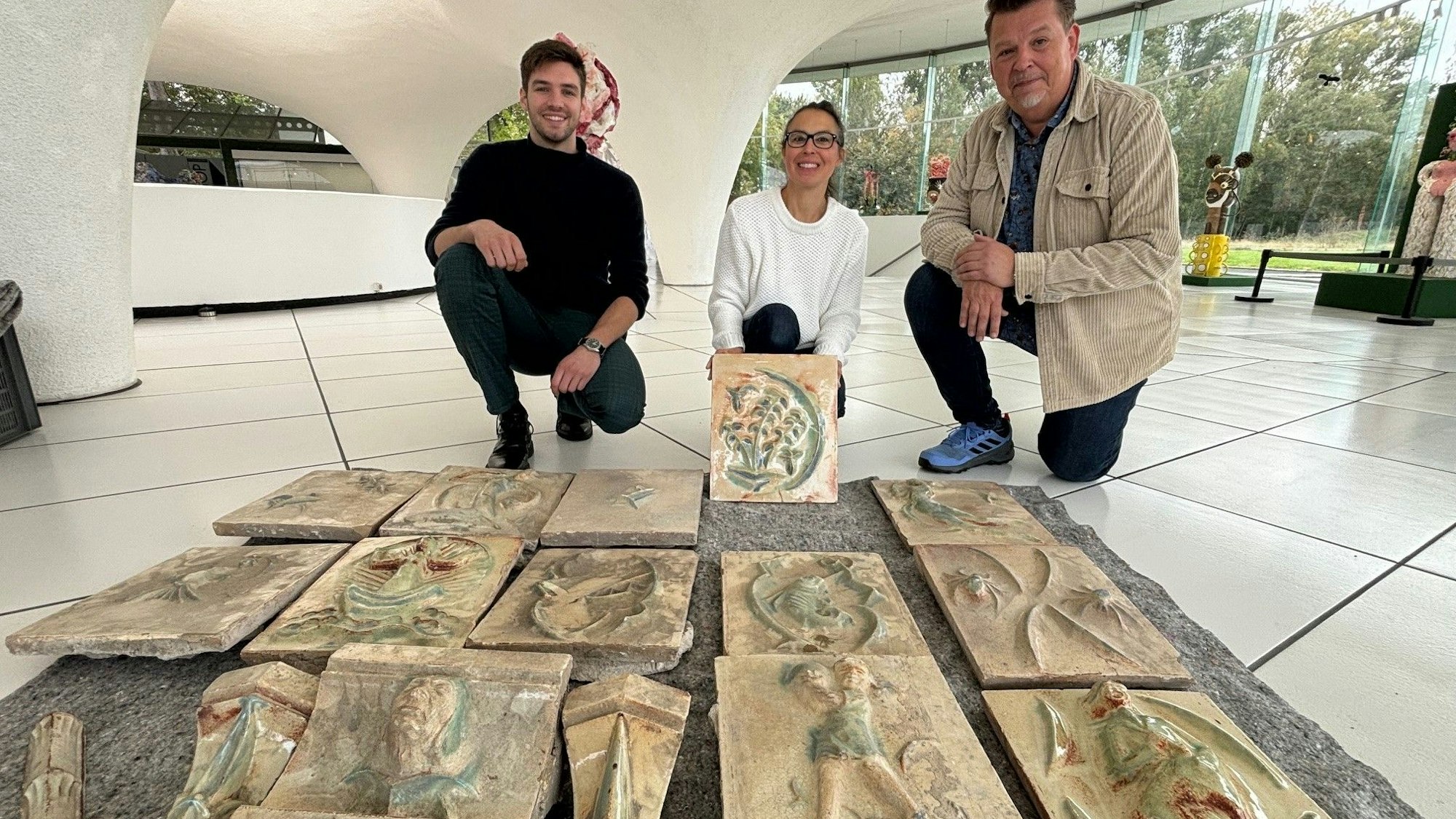 Auf dem Bild sind zwei Männer und eine Frau mit den alten Fliesen im Museum Keramion zu sehen.