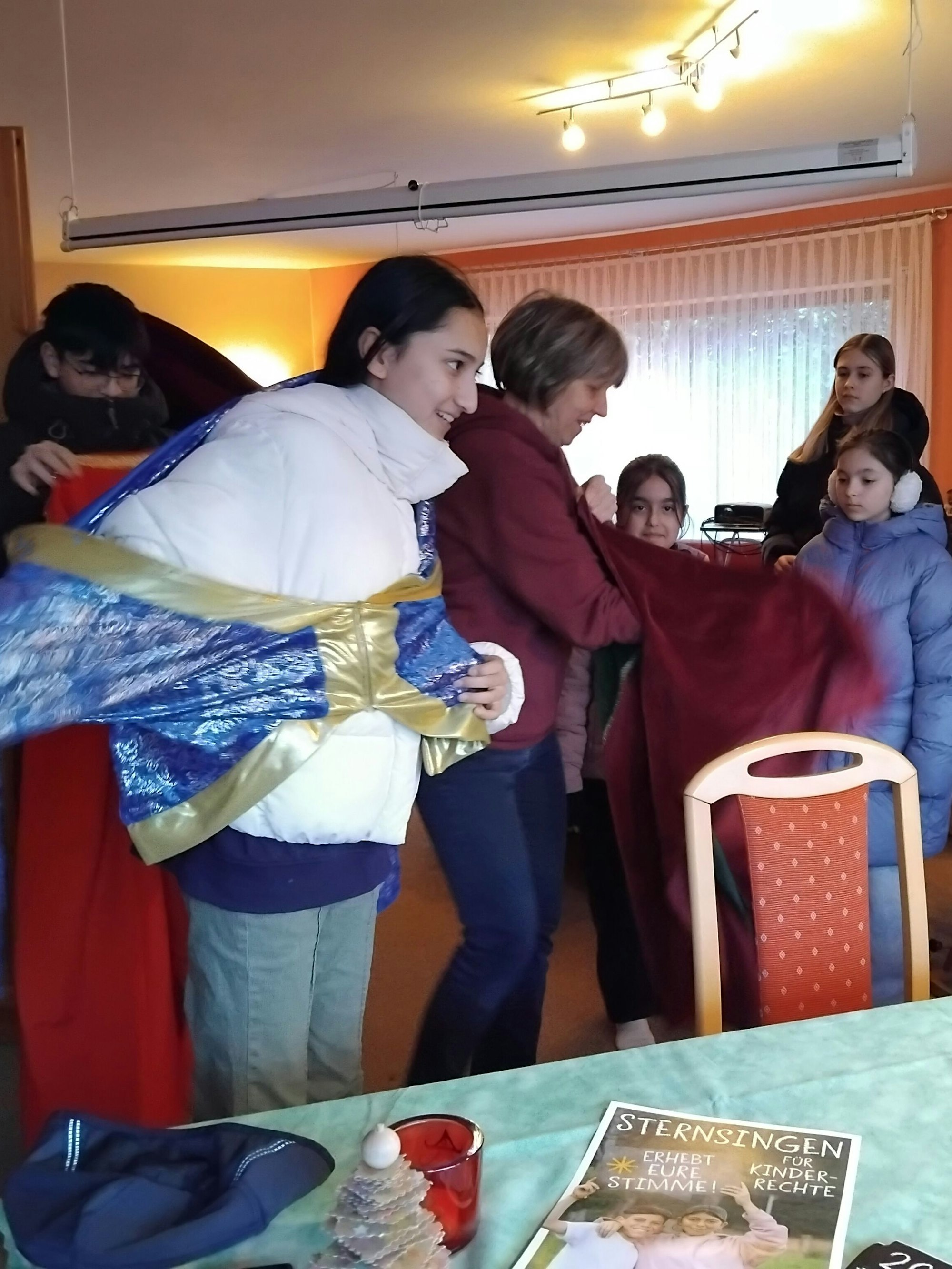 Kinder verkleiden sich als Heilige Drei Könige, eine Frau hilft