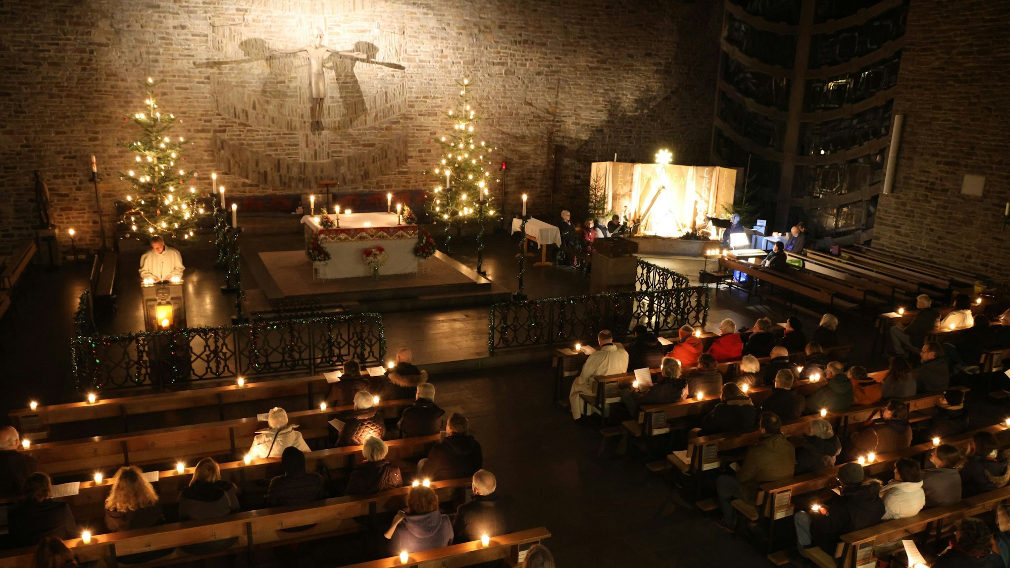 Blick in den Innenraum einer Kirche, in den Bänken sitzen Menschen, Kerzen erhellen den sonst dunklen Innenraum.