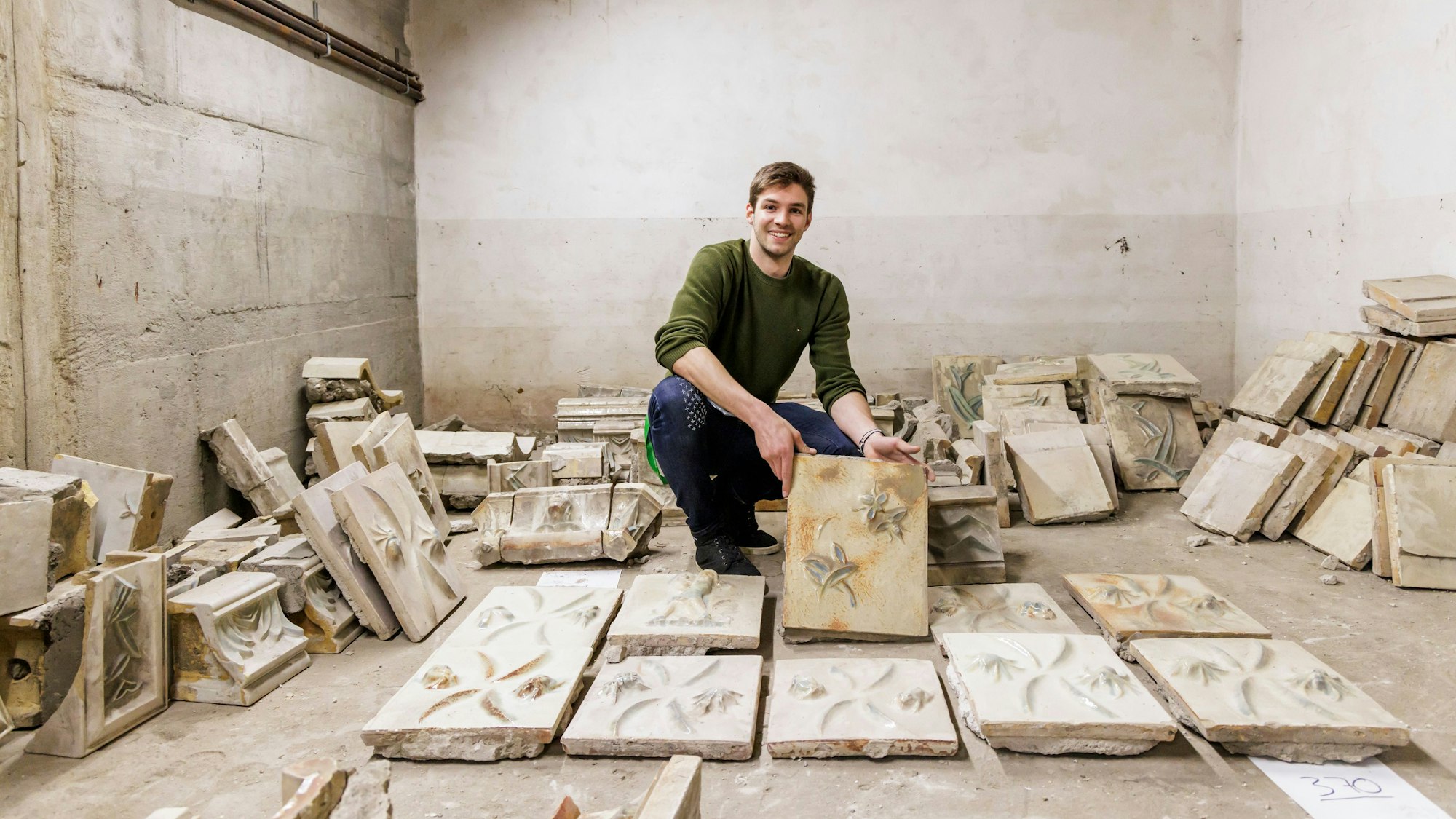 Auf dem Bild ist der Entdecker des Schatzes mit vielen Fliesen in einem Keller zu sehen.