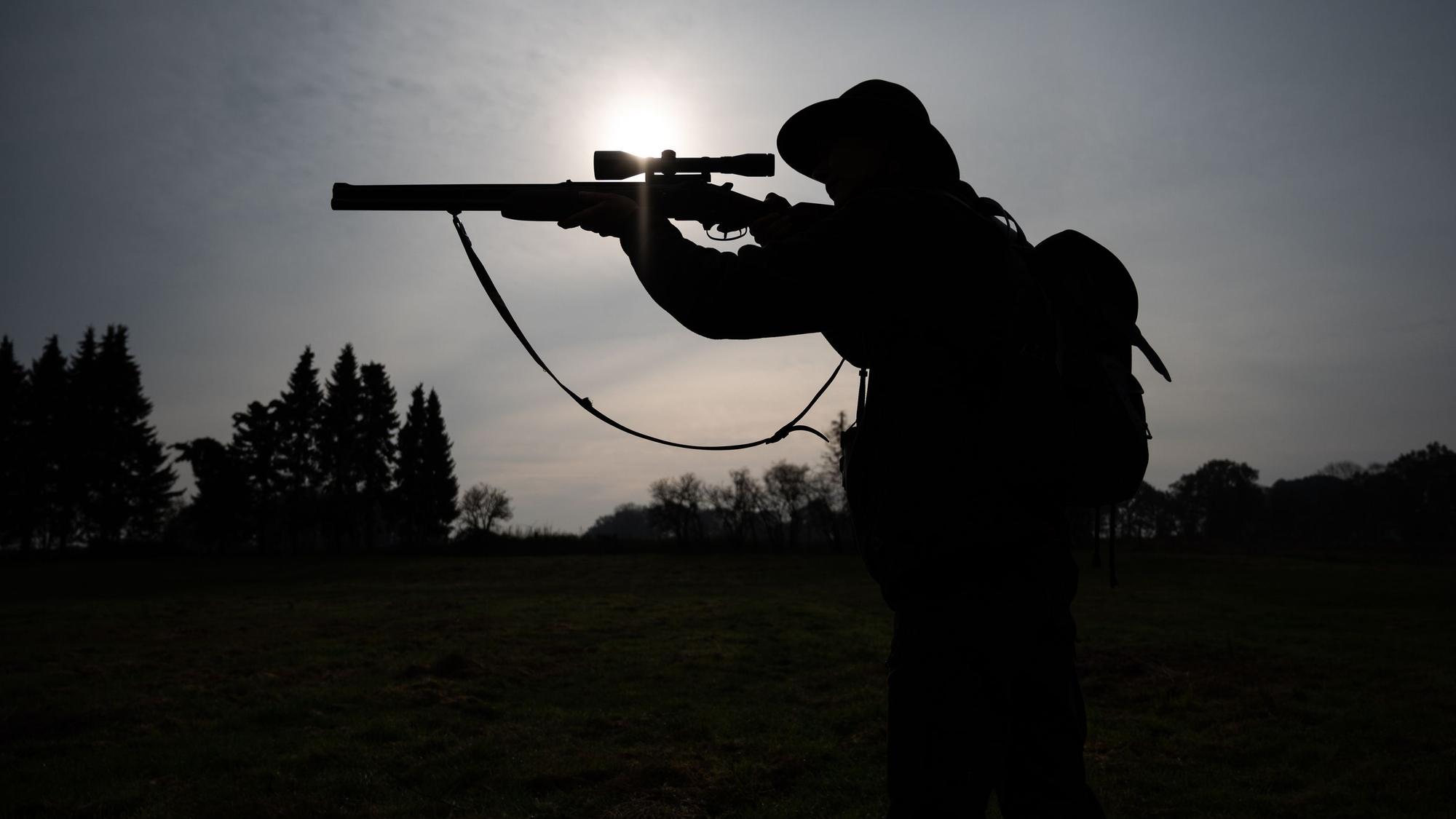 Eine Jägerin steht mit ihrer Bockbüchsflinte auf einer Wiese. (Symbolbild)