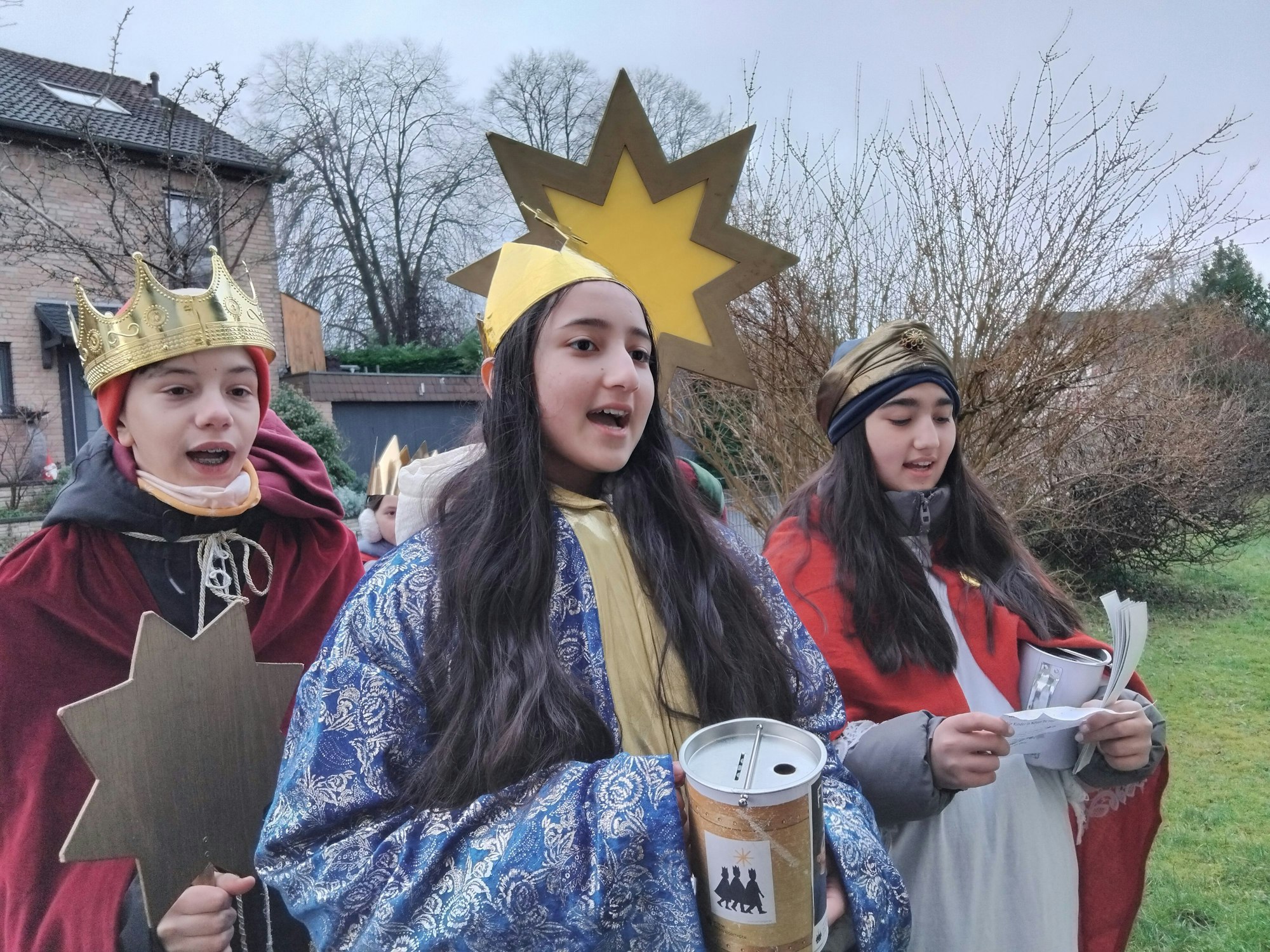 Kinder, verkleidet als Heilige Drei Könige, singen an einer Haustür