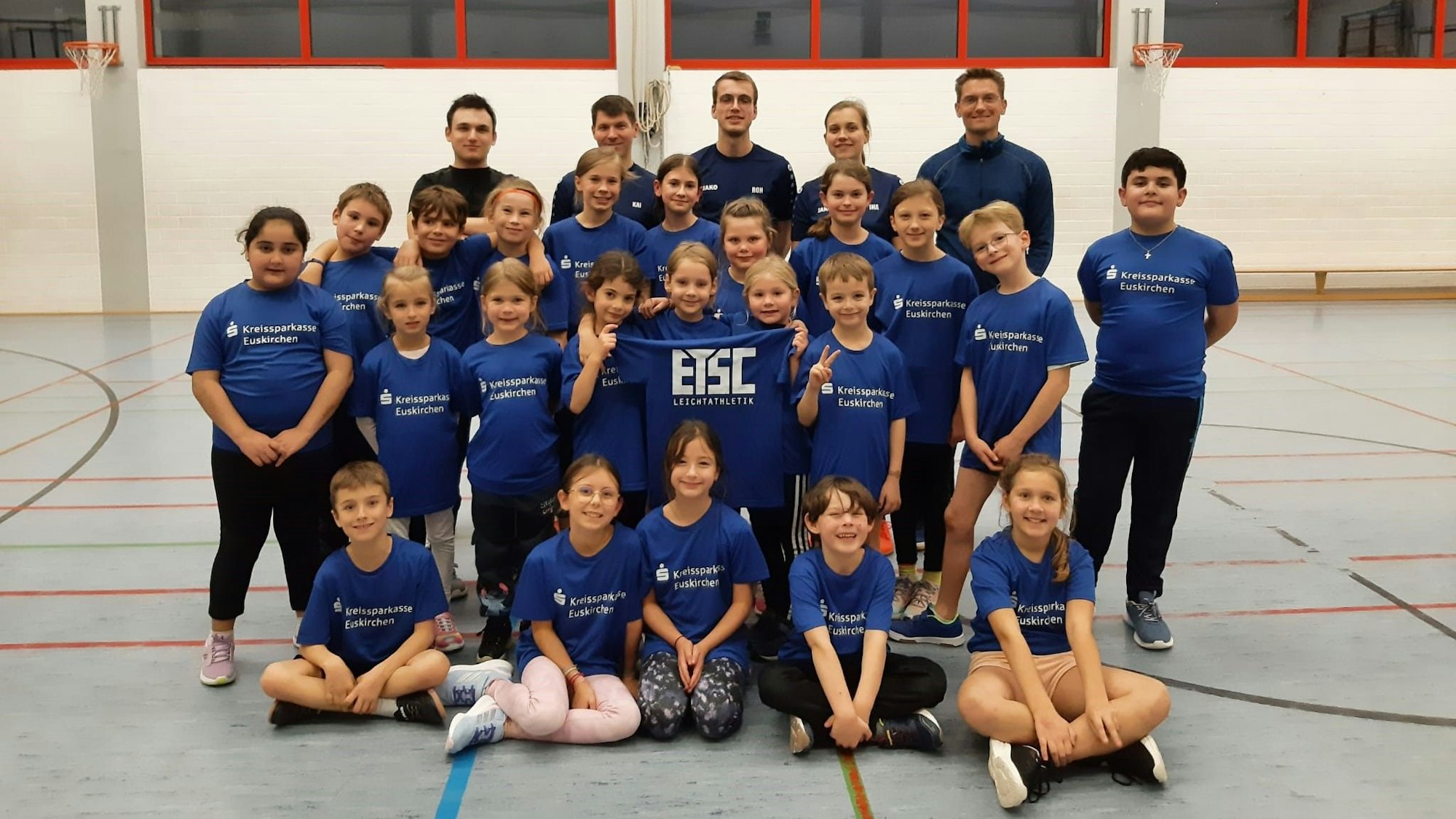 Kinder und Trainer der ETSC-Leichtathletikabteilungen stellen sich auf und halten ein Shirt mit der Aufschrift ETSC hoch.