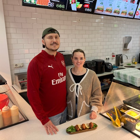 Ein Mann mit Kappe und eine Frau stehen hinter einer Theke, auf der İçli köfte angerichtet wurden.