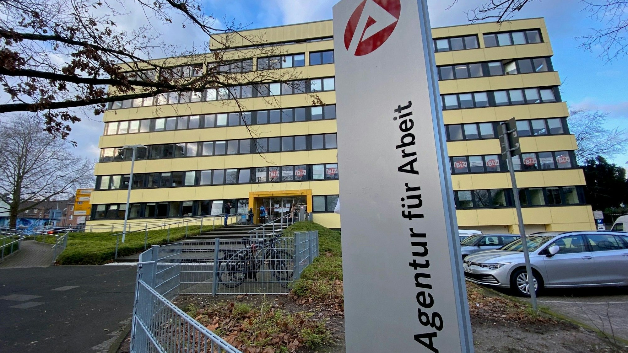 Zu sehen ist das Gebäude der Agentur für Arbeit in Brühl, davor ein großes Schild mit der Aufschrift „Agentur für Arbeit“.