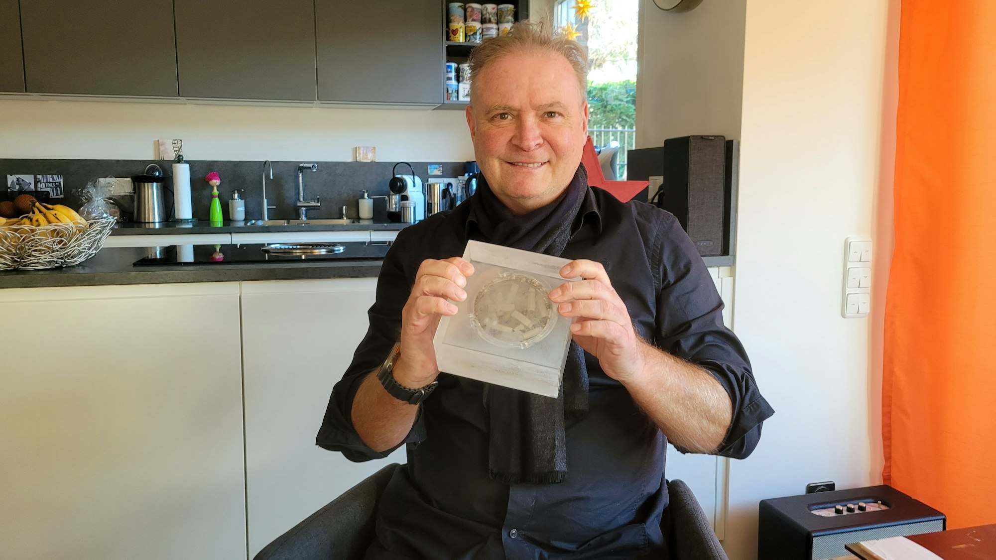 Ein Mann hält einen eingeschweißten Aschenbecher in seinen Händen.