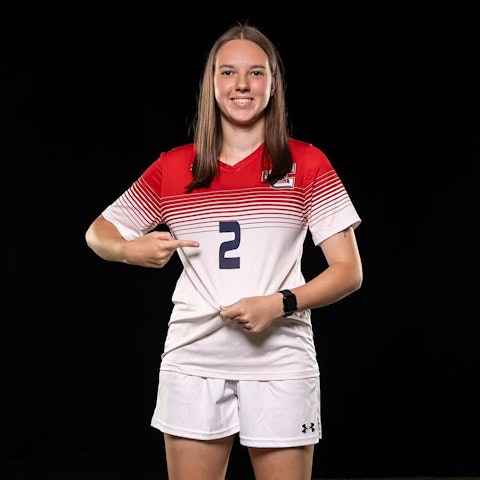 Lena Kücken trägt das Trikot mit der Nummer 2 des Jefferson College. Mit einem Finger zeigt sie auf die Nummer, mit der anderen Hand zieht sie das Trikot straff.