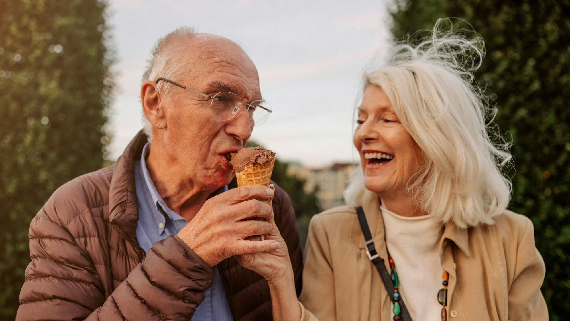 Eine ältere lachende Frau hält einem älteren Mann ein Eis an den Mund