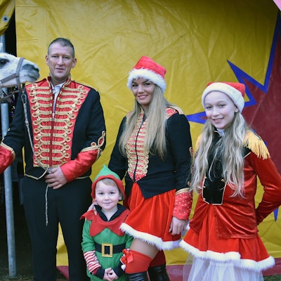 Eine Zirkusfamilie steht mit einem Lama vor einem Zirkuszelt.