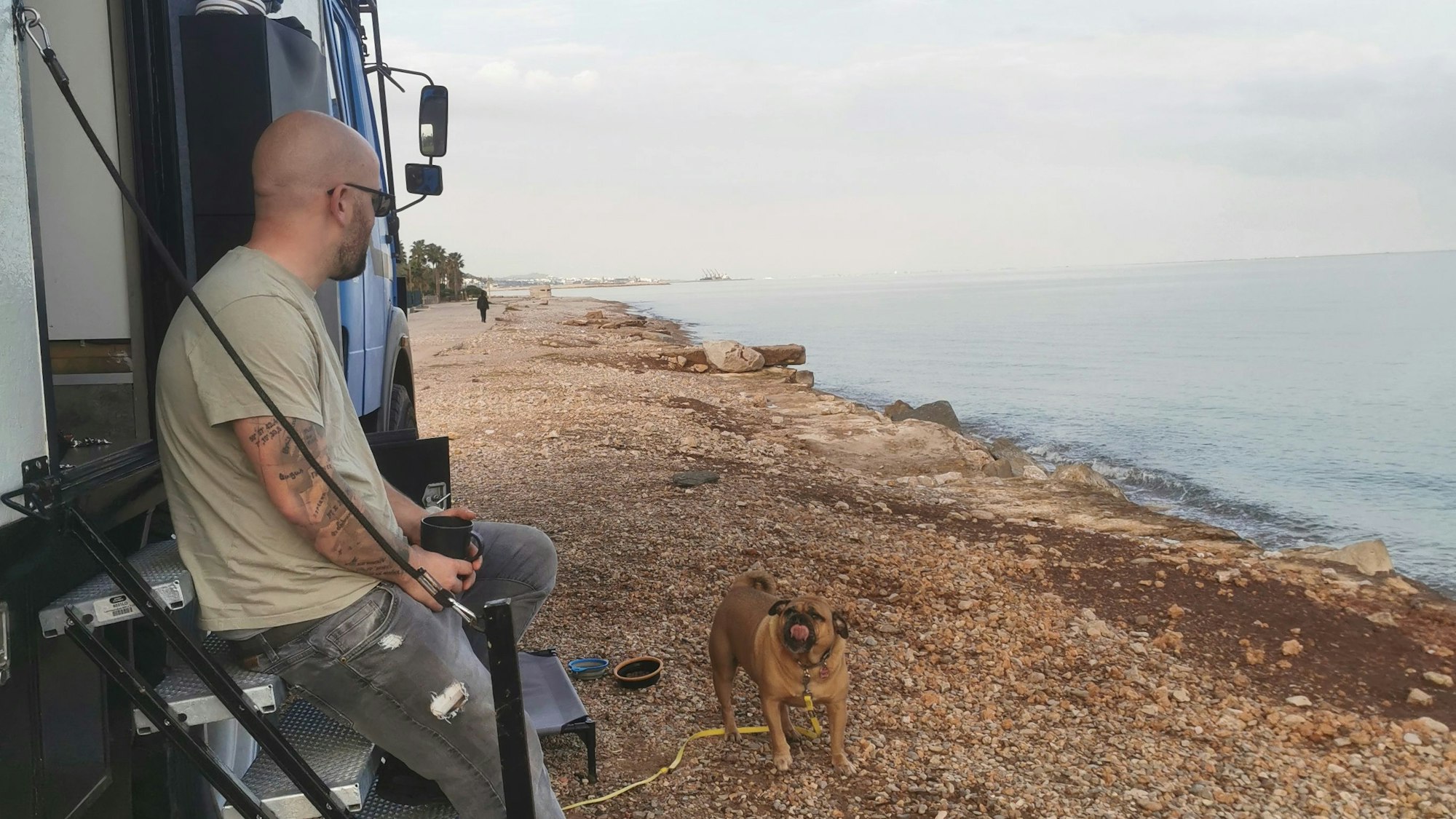 Ein Mann sitzt auf der Treppe eines Expeditionsmobils und schaut aufs Meer.