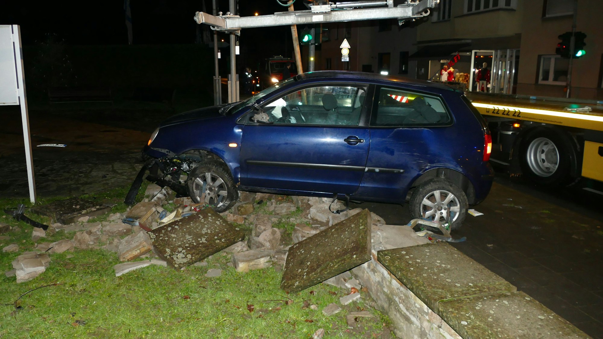 Ein blauer Polo steht auf den Trümmern einer kleinen Mauer. Ein Abschleppwagen steht im Hintergrund.
