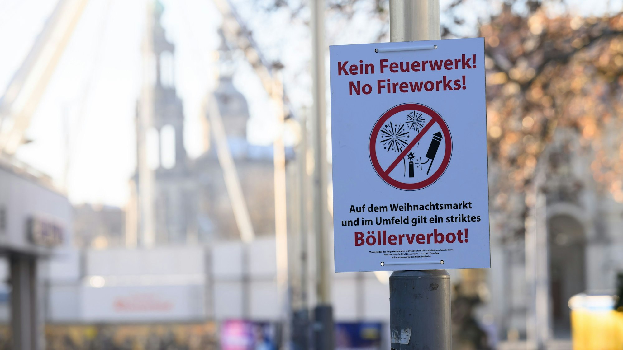 31.12.2024, Sachsen, Dresden: Ein Schild ·Böllerverbot· hängt auf dem Weihnachtsmarkt ·Augustusmarkt· auf der Hauptstraße an einem Lichtmast, dahinter ist die Altstadt zu sehen. Foto: Robert Michael/dpa +++ dpa-Bildfunk +++