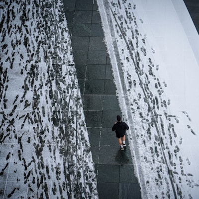 In kurzen Hosen läuft ein Jogger über einen verschneiten Gehweg.