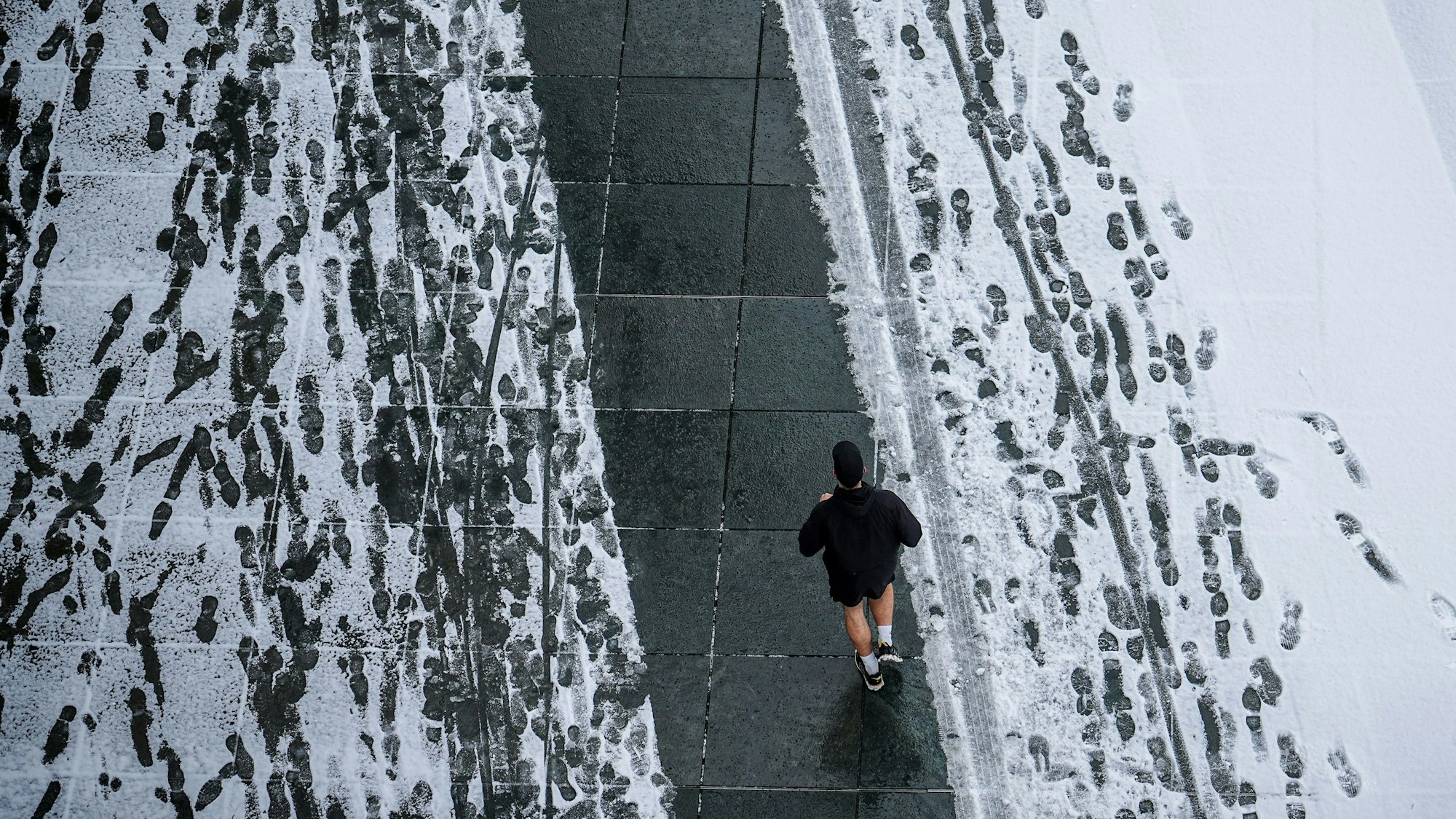 In kurzen Hosen läuft ein Jogger über einen verschneiten Gehweg.