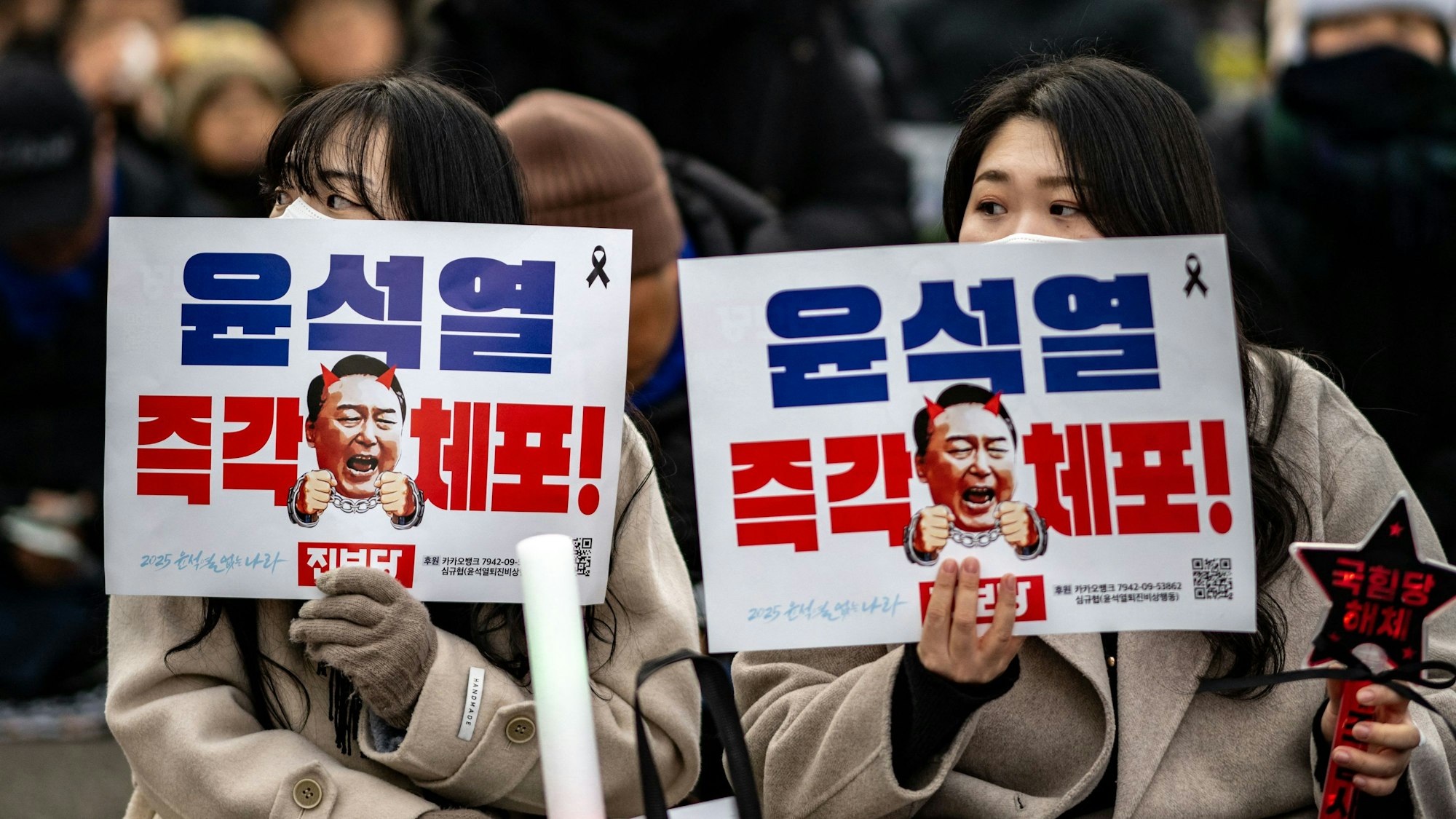 Menschen halten Plakate mit der Aufschrift „Verhaftet Yoon Suk Yeol sofort“ hoch.