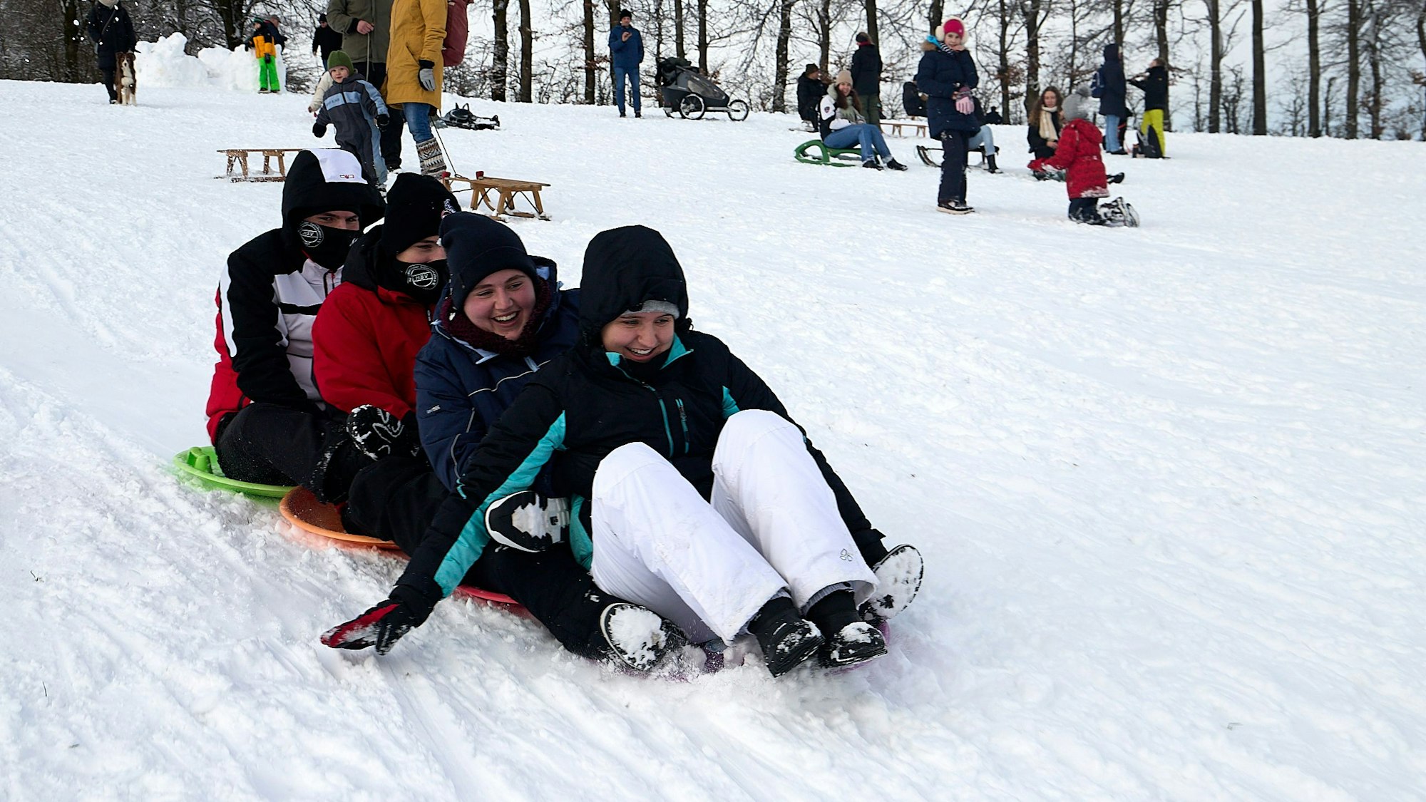 Die vier Kinder rodeln mit einem Vierer-Bob den Abhang hinunter.