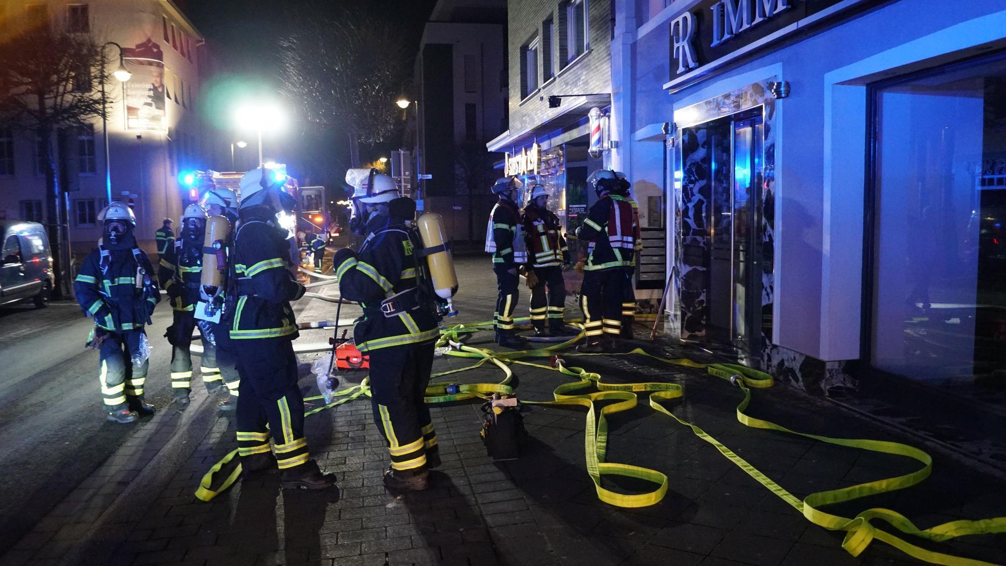Feuerwehrleute stehen in der Dunkelheit vor einem Gebäude in Euskirchen, in dem es gebrannt hat.