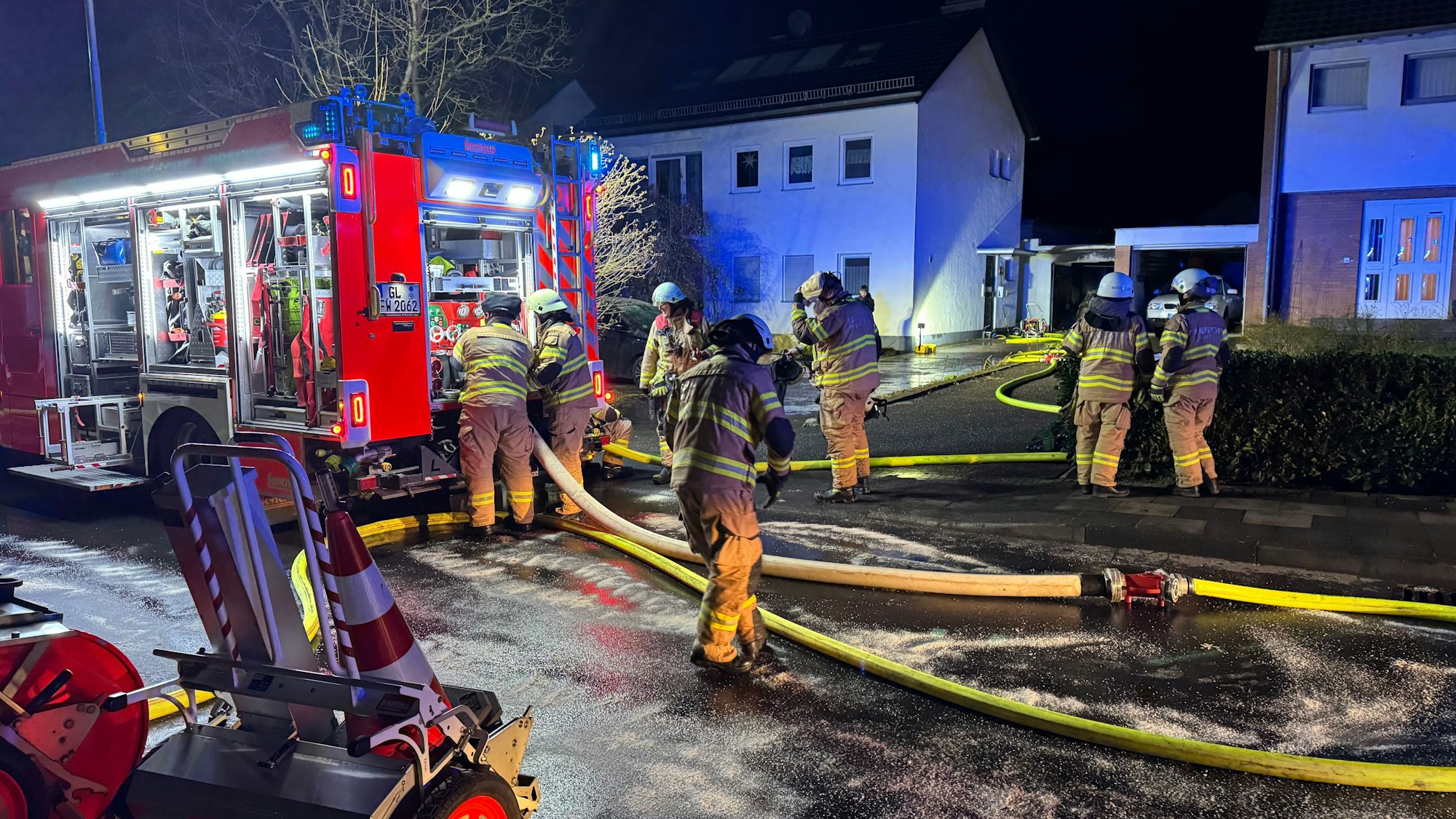 Feuerwehrleute haben Schläuche auf dem Neuenweg verlegt, ein Feuerwehrfahrzeug steht vor einem Haus.