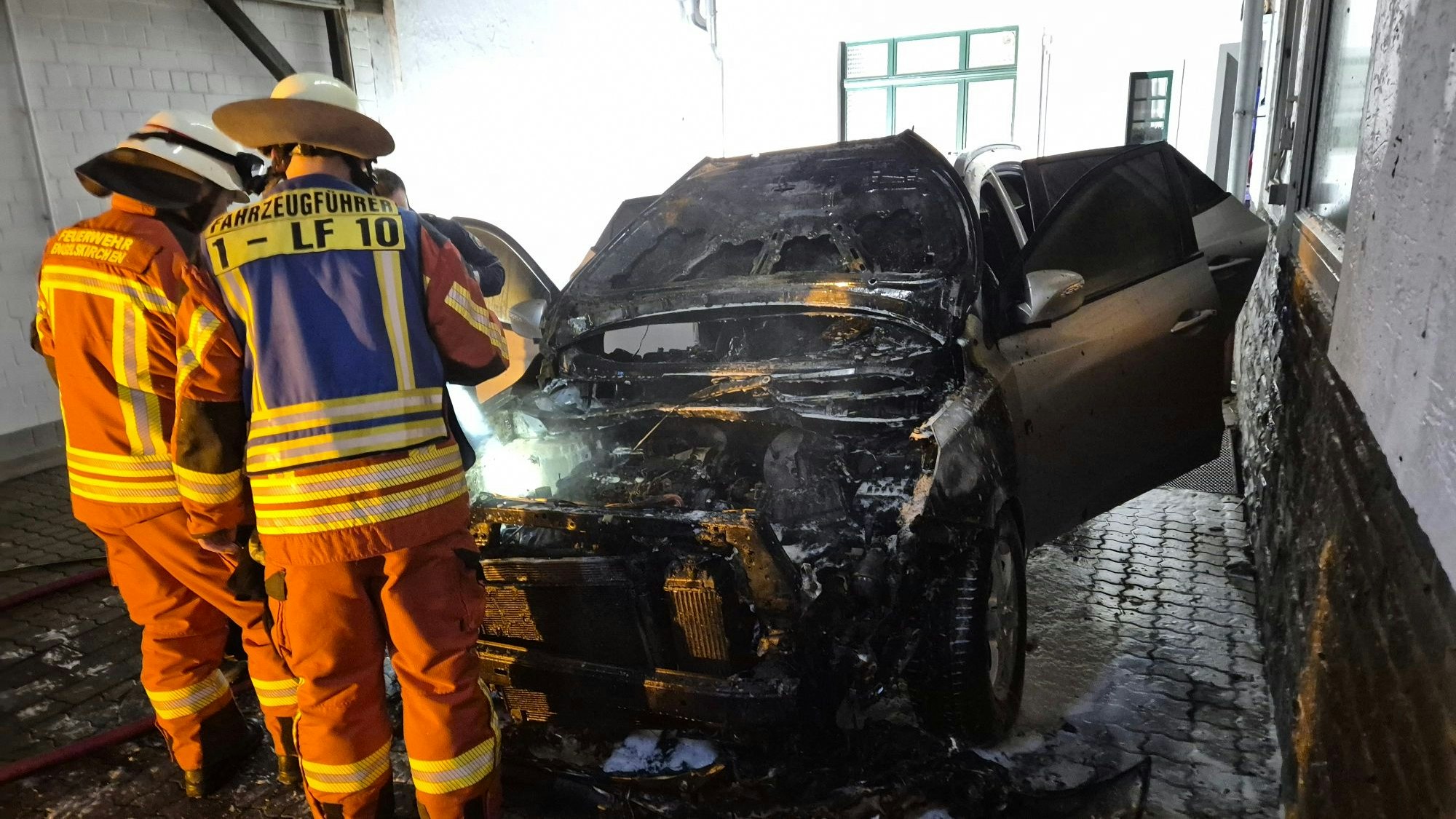 Zwei Feuerwehrleute begutachten das Wrack eines ausgebrannten Autos.