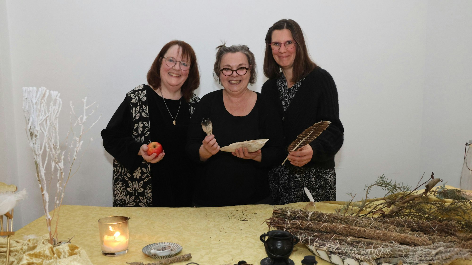 Drei Frauen stehen hinter einem Tisch voller Naturmaterialien, die sich zum Räuchern eignen.