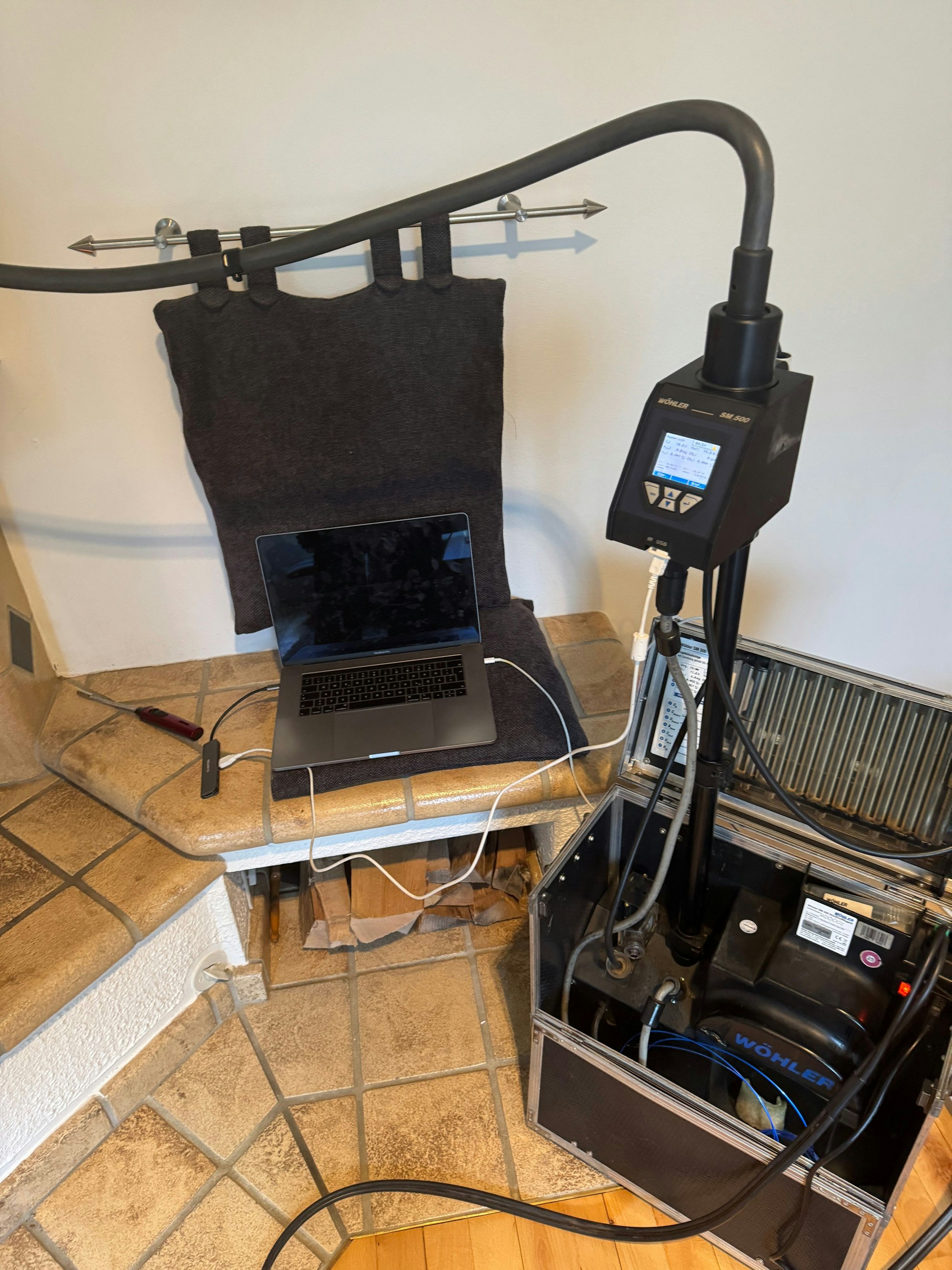 Eine Messapparatur mit Laptop und digitalem Display vor einem Kaminofen.