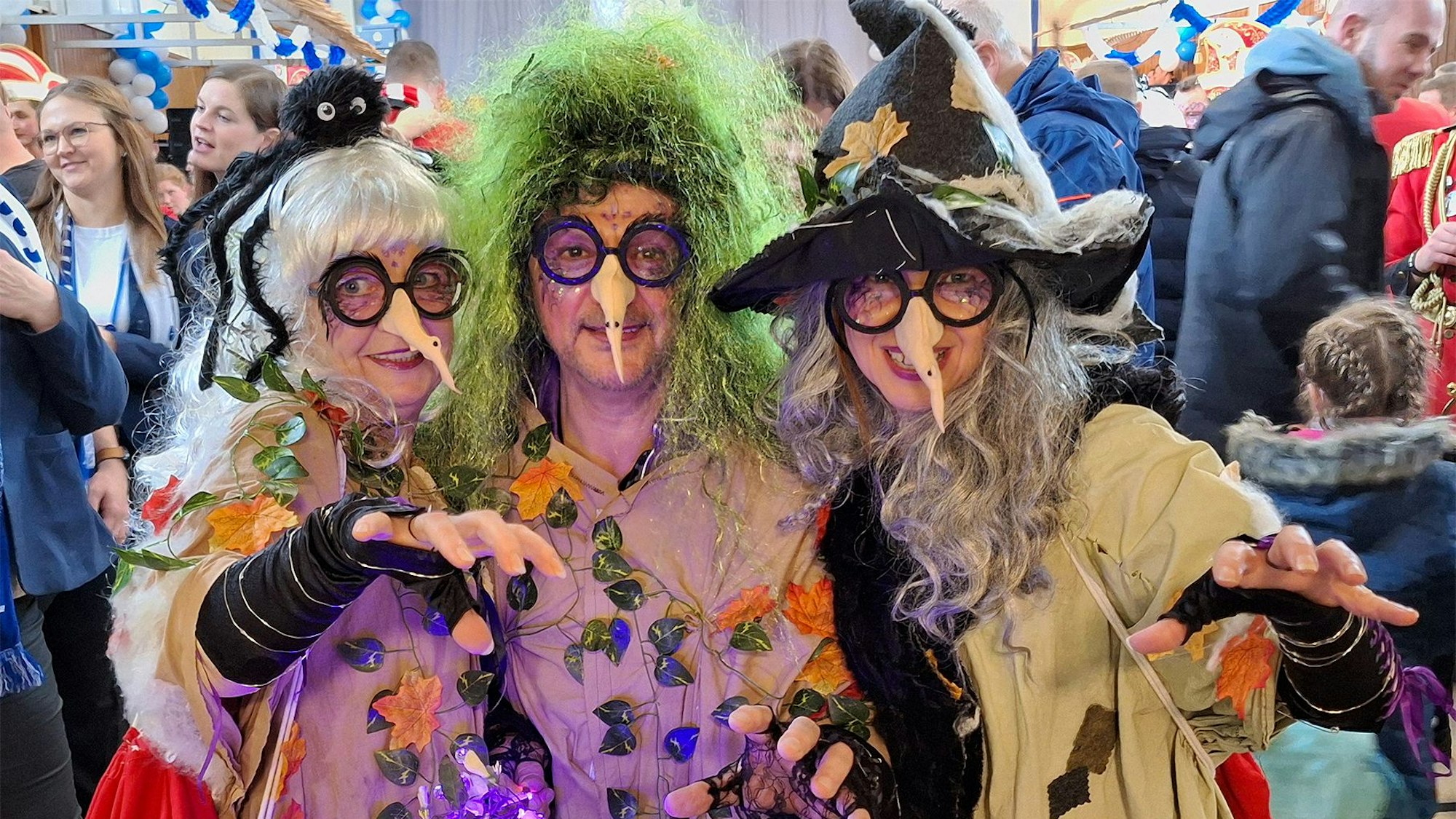 Drei bunt als Hexen kostümierte Frauen strecken ihre Hände in Richtung Fotograf aus.