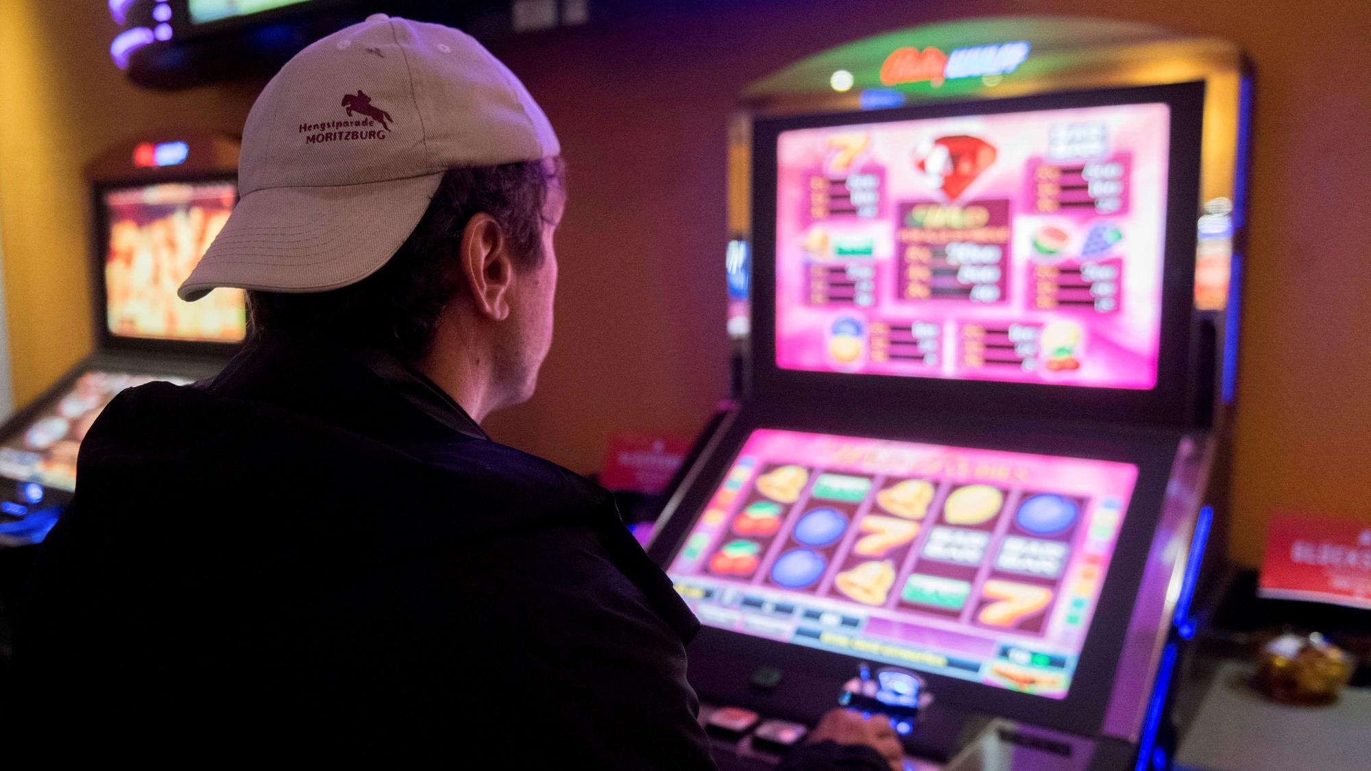Ein Mann mit Baseballkappe sitzt mit dem Rücken zur Kamera an einem Spielautomaten.