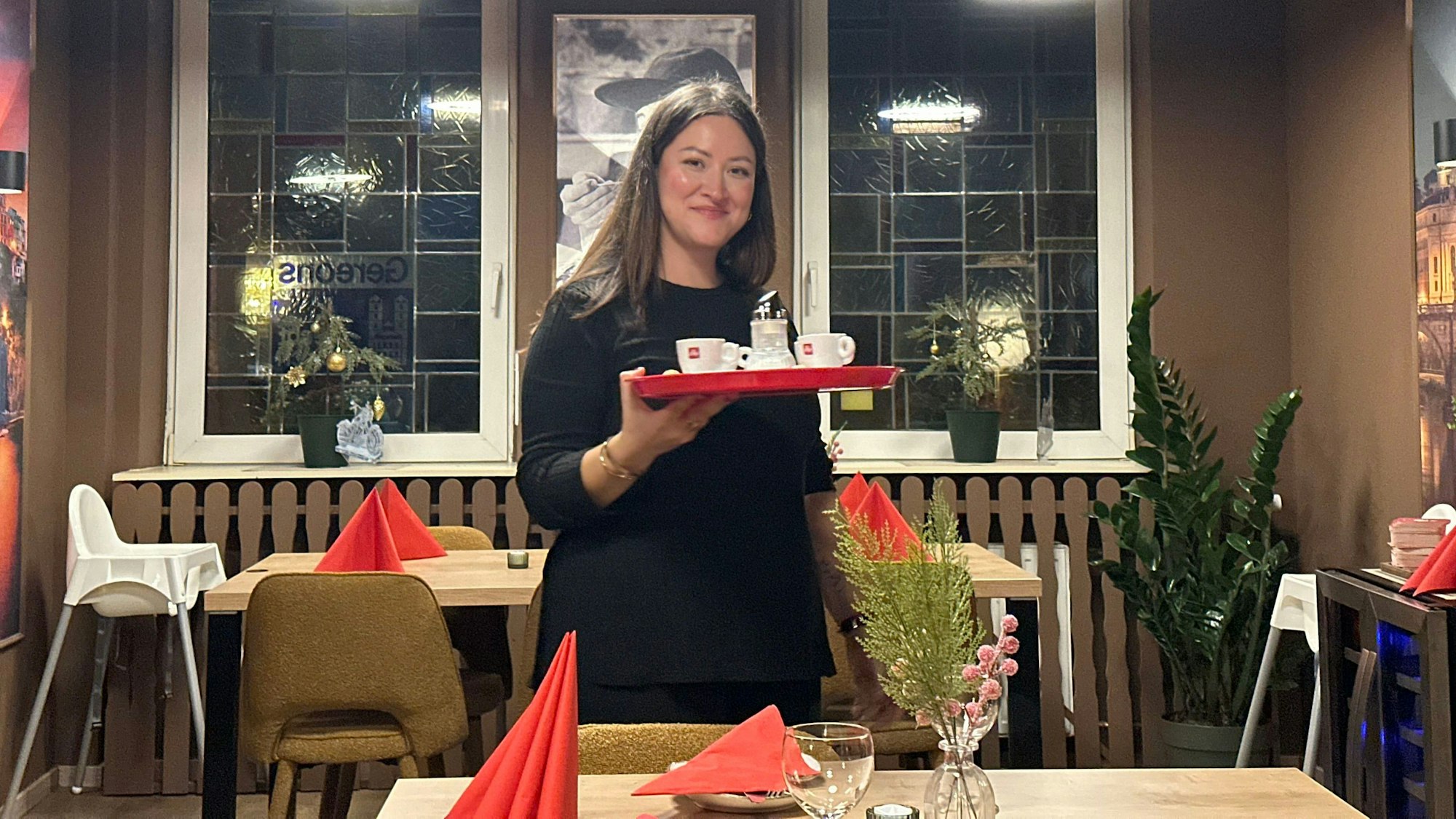 Eine Frau mit dunklen Haaren hält ein Tablett in der Hand, auf dem Espresso-Tassen stehen. Sie steht im Gastraum des Restaurants Buon Cibo in Köln-Zündorf.