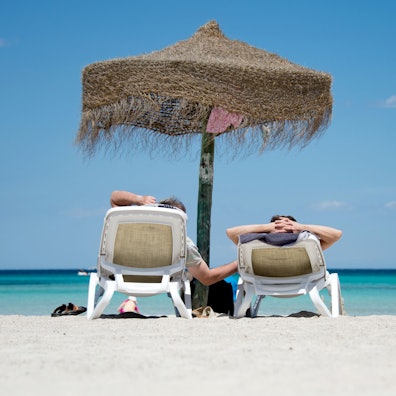 Zwei Menschen sitzen unter einem Sonnenschirm am Strand.