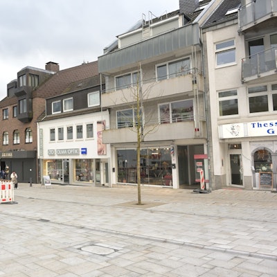 Geschäfte, die Baustelle in der Mitte der Straße sowie das neue Granitpflaster sind zu sehen.