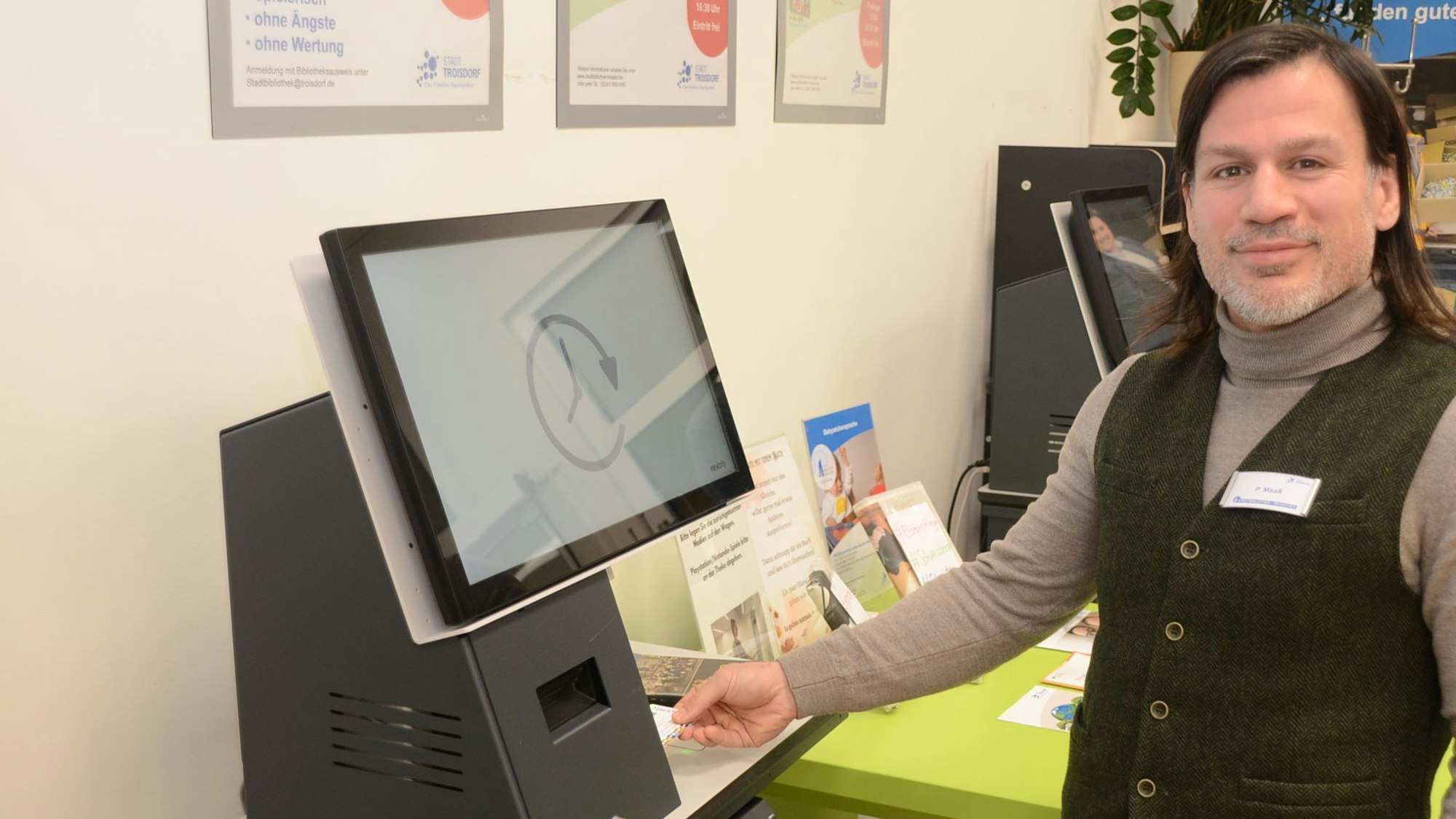 Ein Mann in Weste und Pullover steht an einem Computerterminal.
