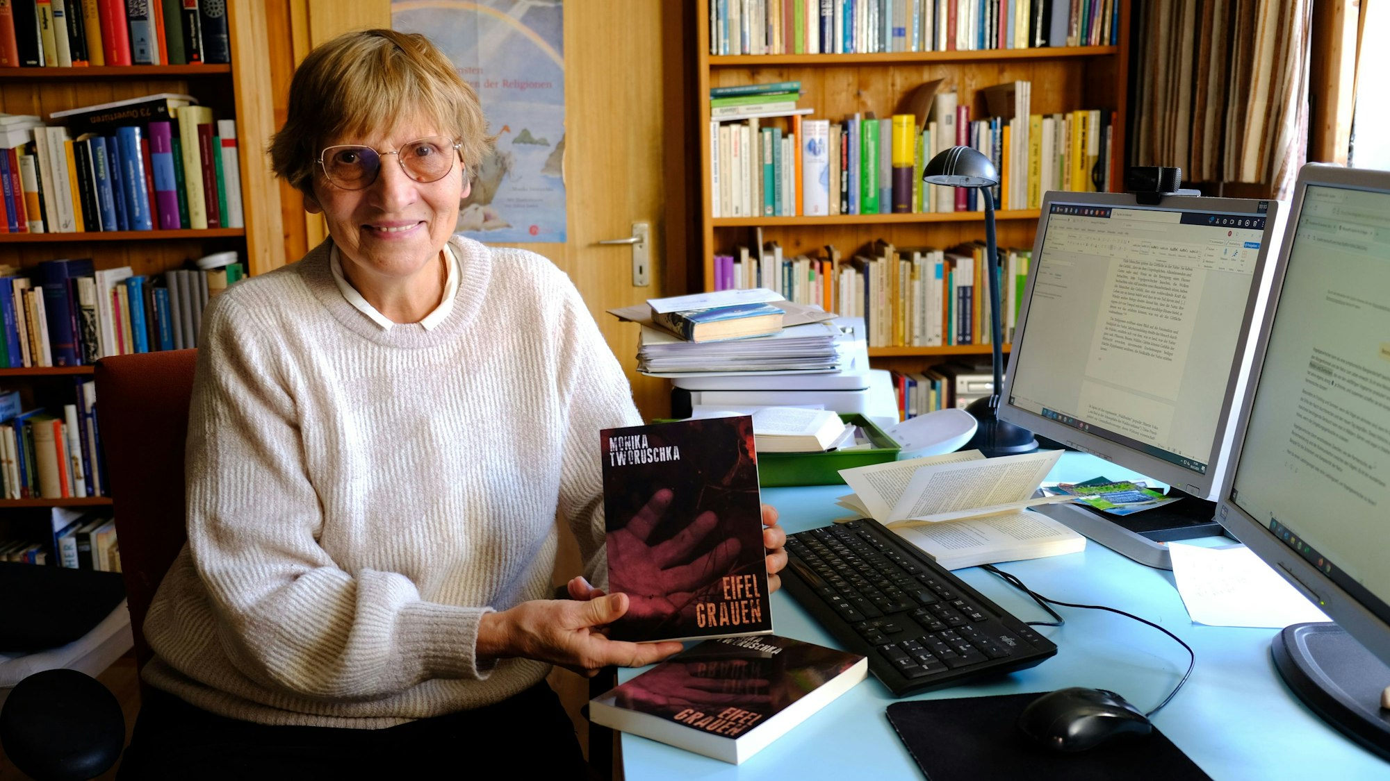 Die Autorin Monika Tworuschka aus Arloff sitzt am Schreibtisch ihres Arbeitszimmers und hält ihren ersten Kriminalroman „Eifel-Grauen“ in die Kamera.