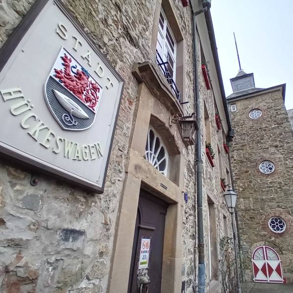 Vorn ein steinernes Wappen mit der Aufschrift Stadt Hückeswagen, im Hintergrund das Schloss.