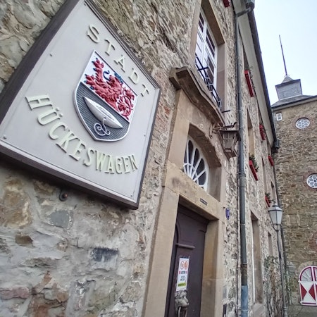 Vorn ein steinernes Wappen mit der Aufschrift Stadt Hückeswagen, im Hintergrund das Schloss.
