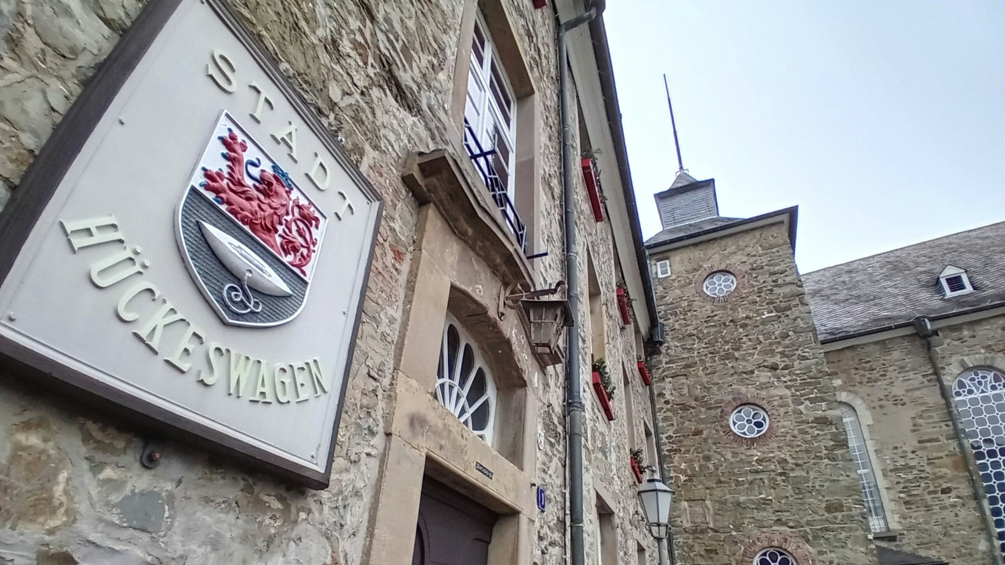 Vorn ein steinernes Wappen mit der Aufschrift Stadt Hückeswagen, im Hintergrund das Schloss.